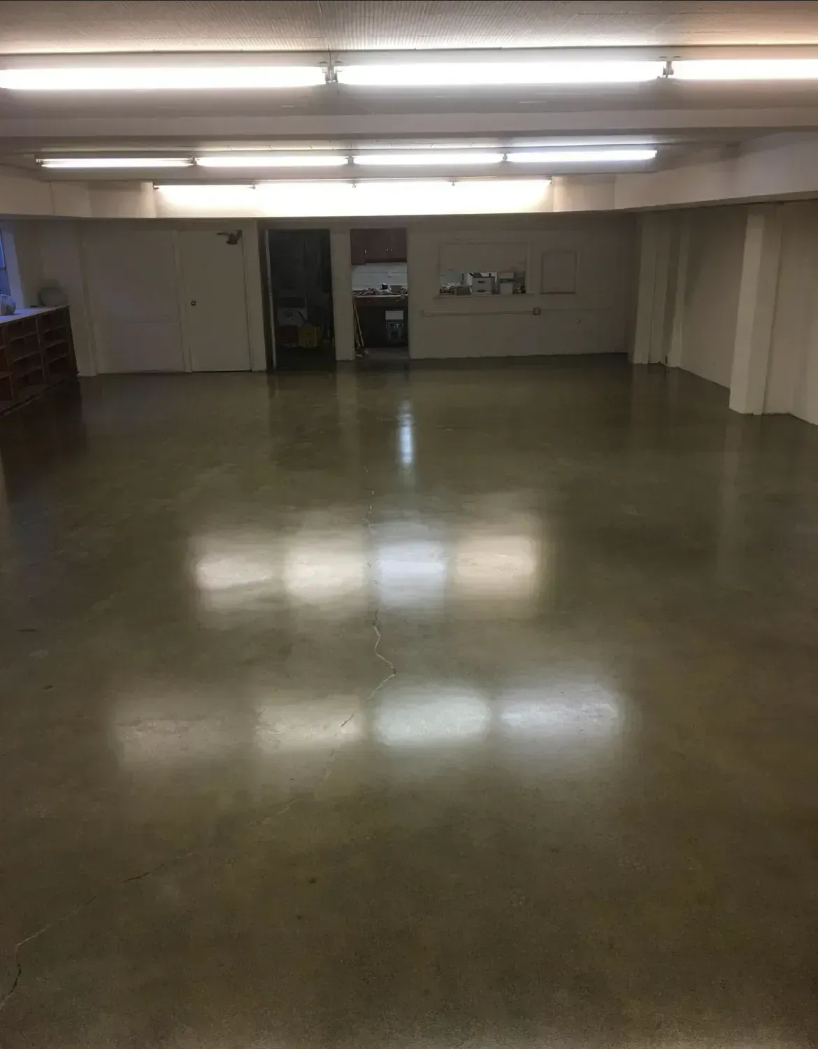 Empty room with polished concrete floor, bright overhead lights, and a small doorway.