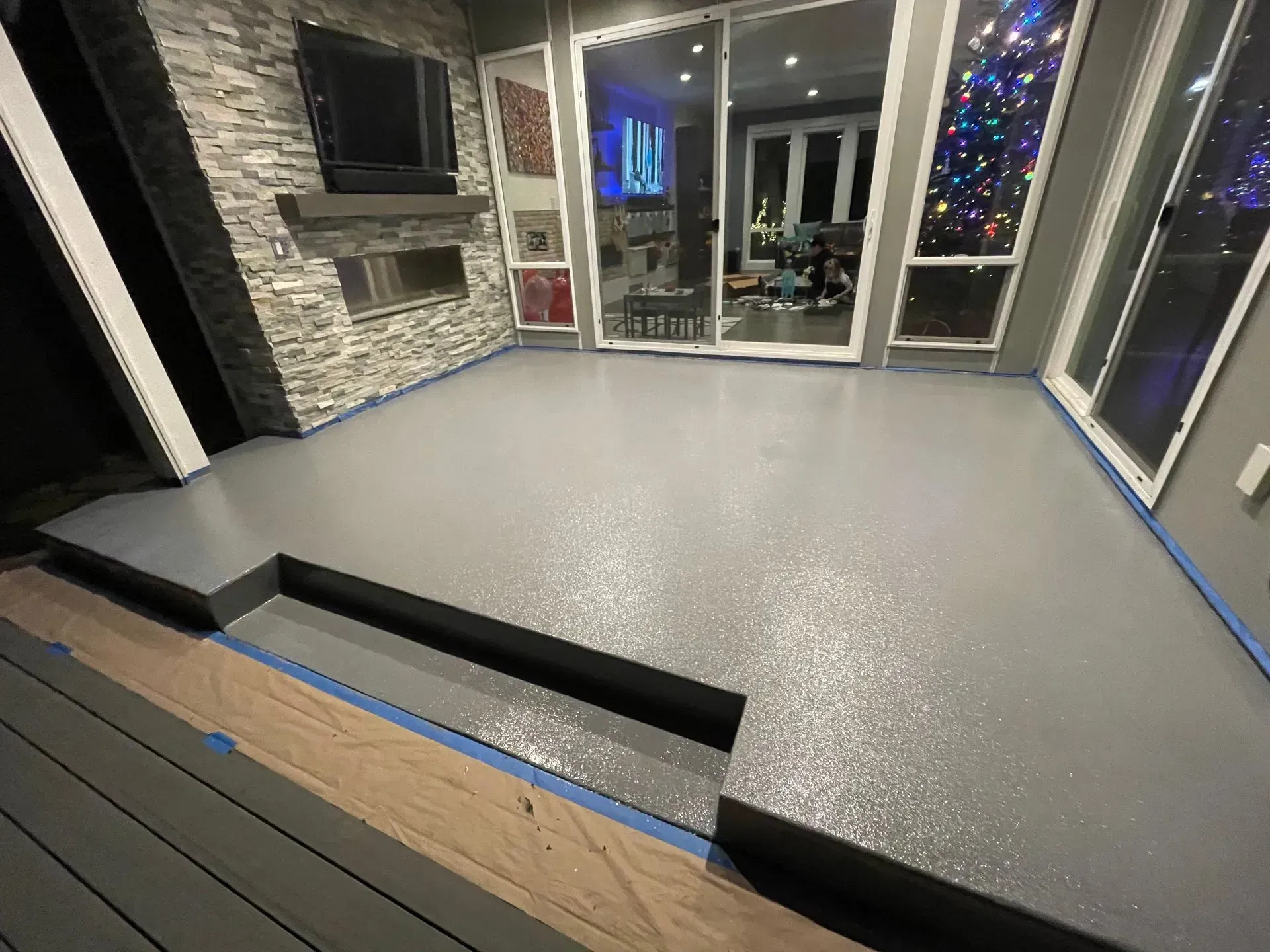 Newly coated gray patio with stone wall, sliding glass doors, and steps.