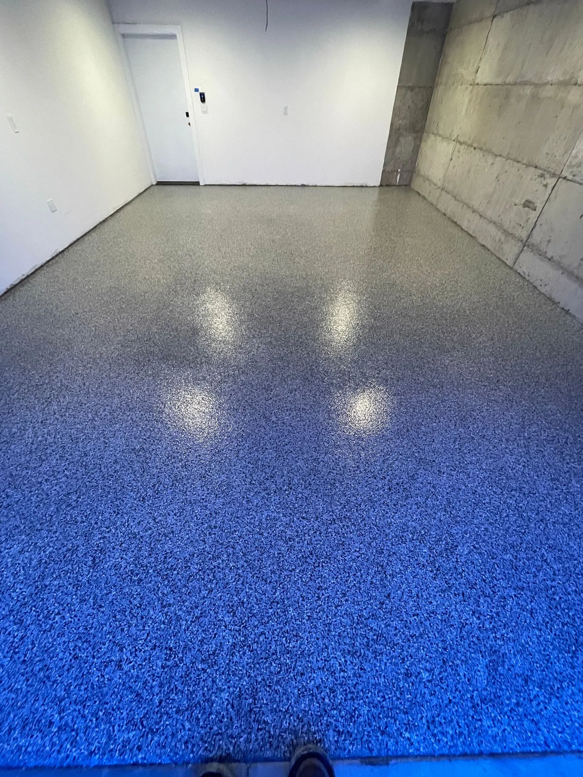 Epoxy-coated floor in a room with white walls and a concrete wall.