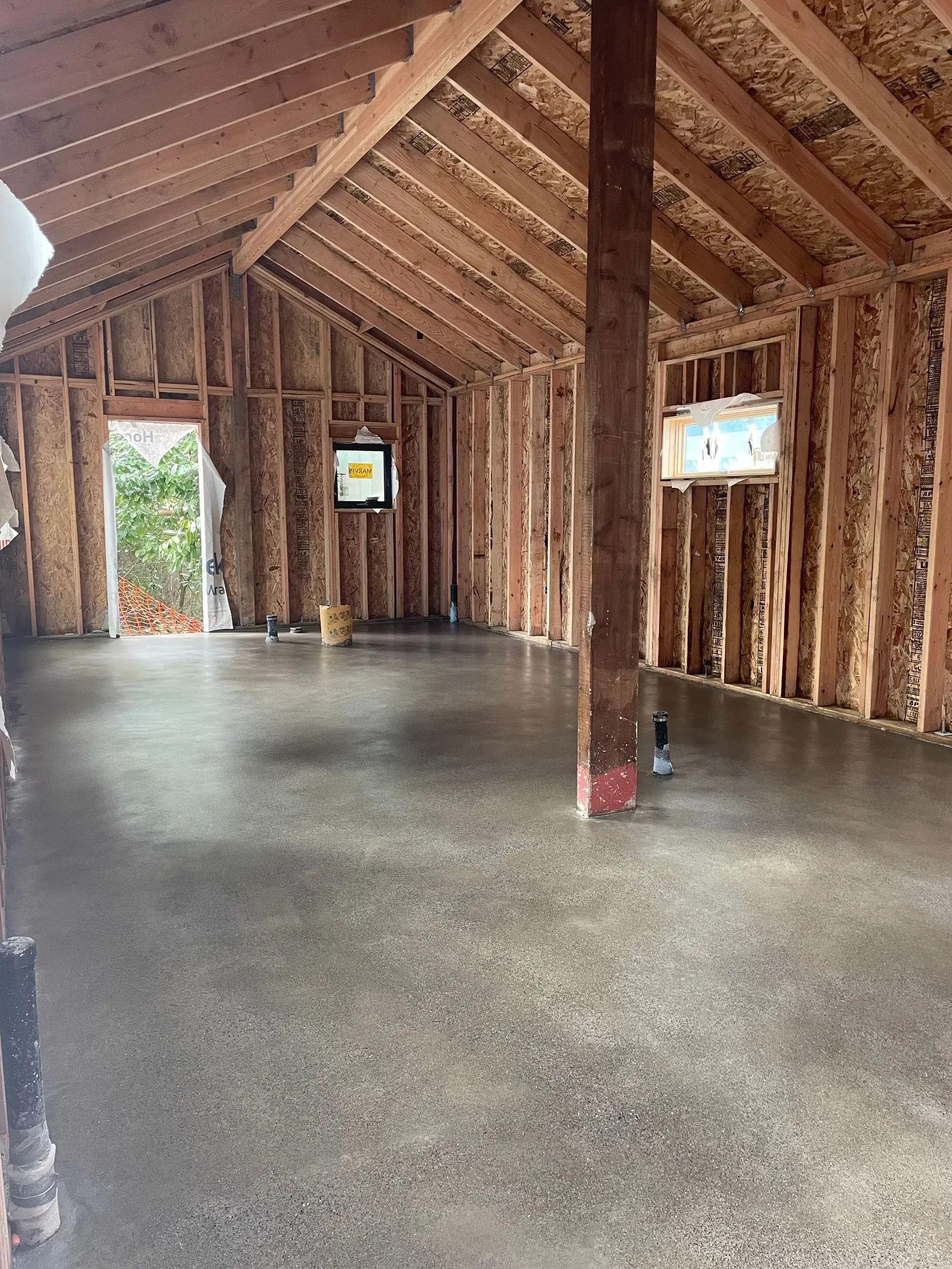 Interior of a wooden framed building with a polished concrete floor. Walls are bare. Light streams in from the doorway.