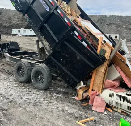 Dump truck unloading debris, including wood and insulation, onto a dirt surface.