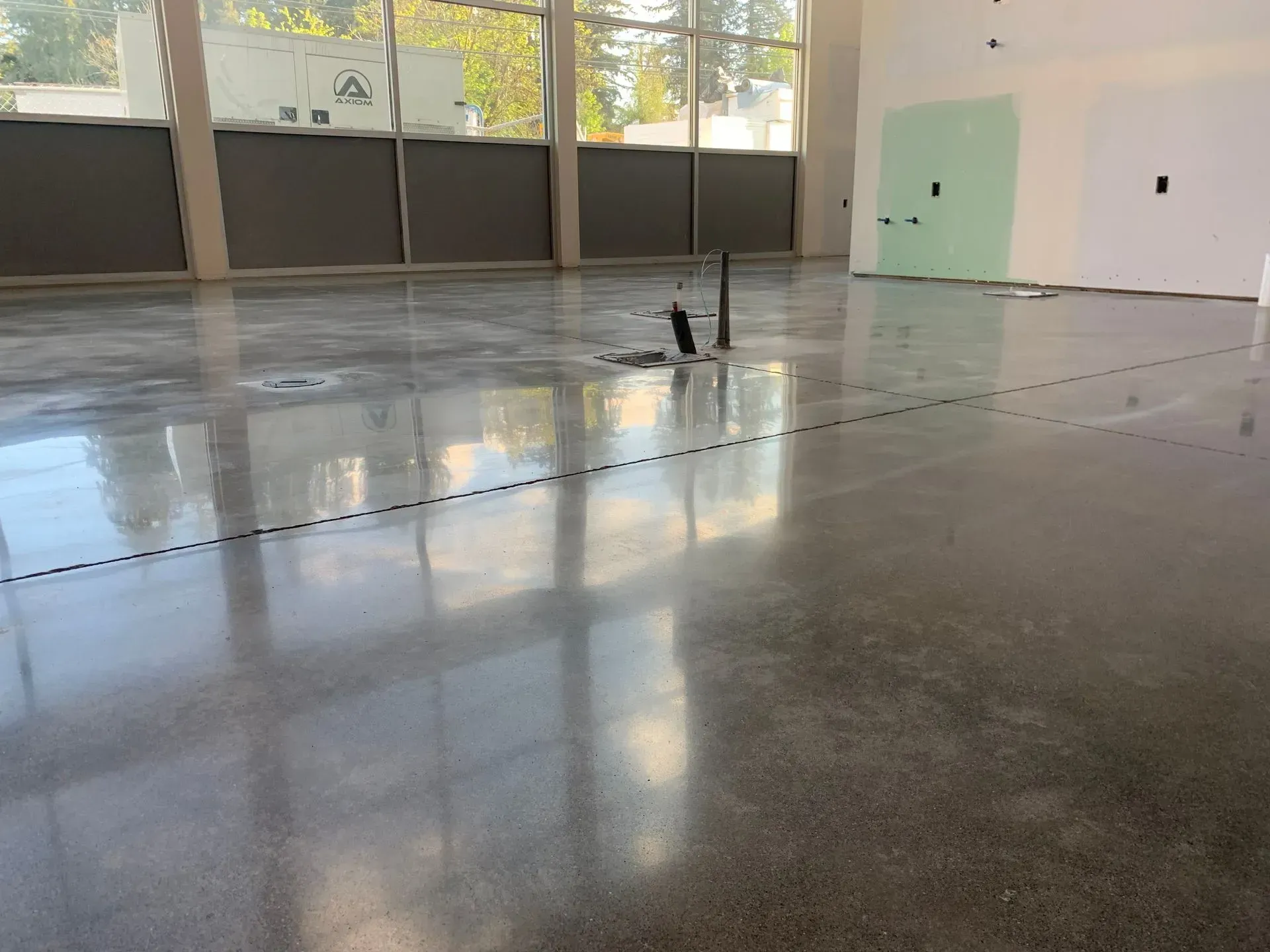 Polished concrete floor in an unfinished room, with window reflections and exposed plumbing pipes.