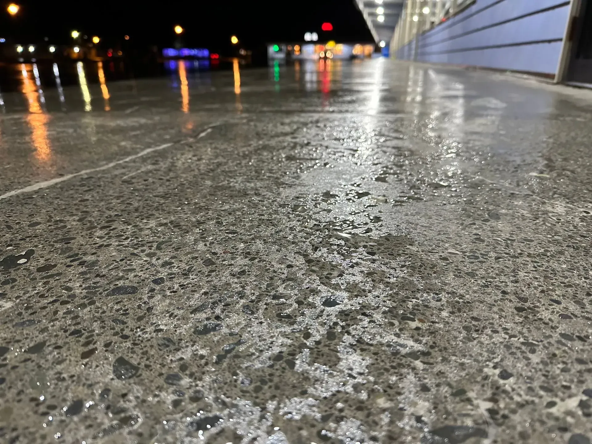 Wet concrete floor with city lights reflecting in the puddles at night.