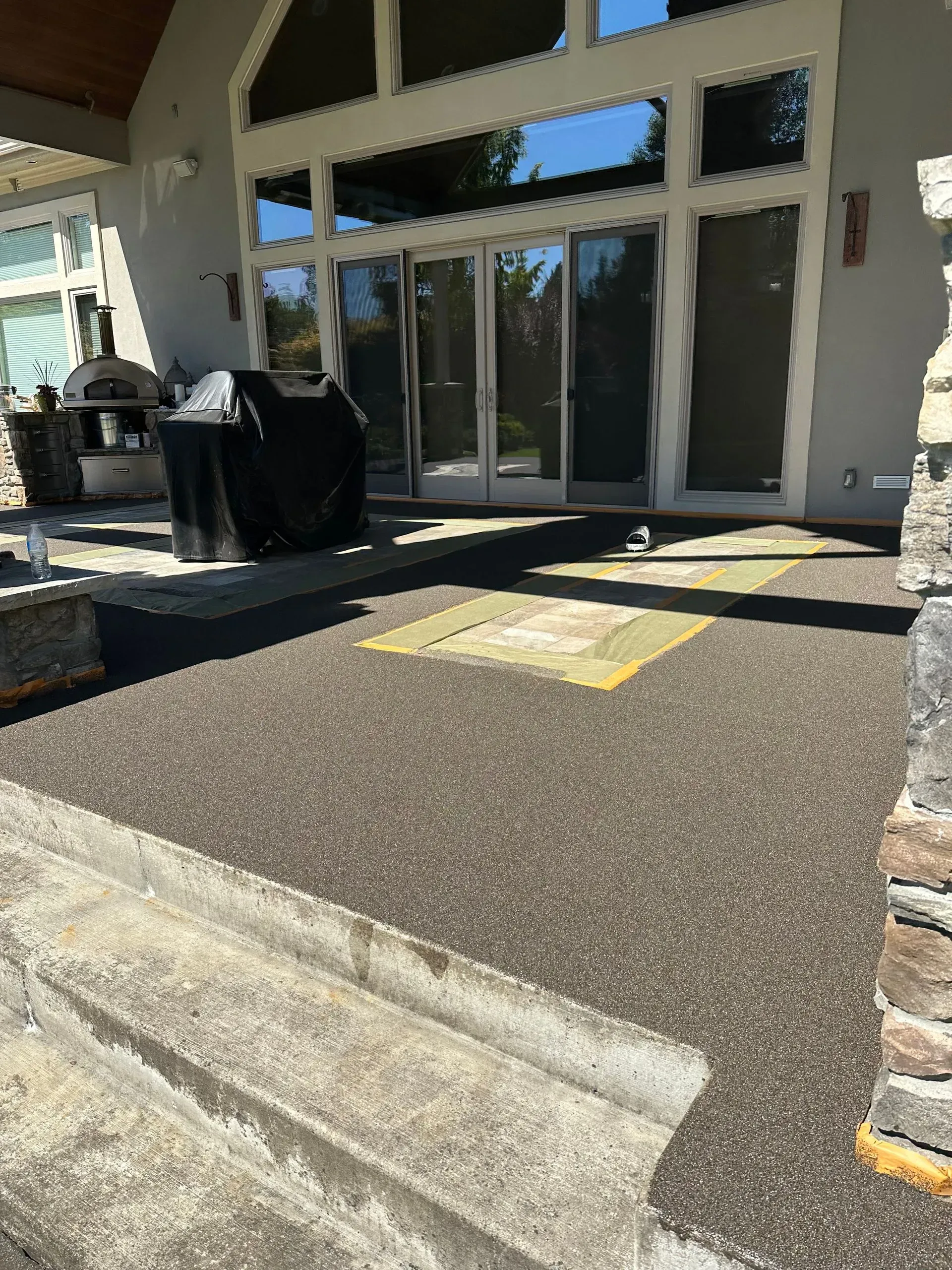 Dark speckled patio with steps, leading to a home with large glass doors.