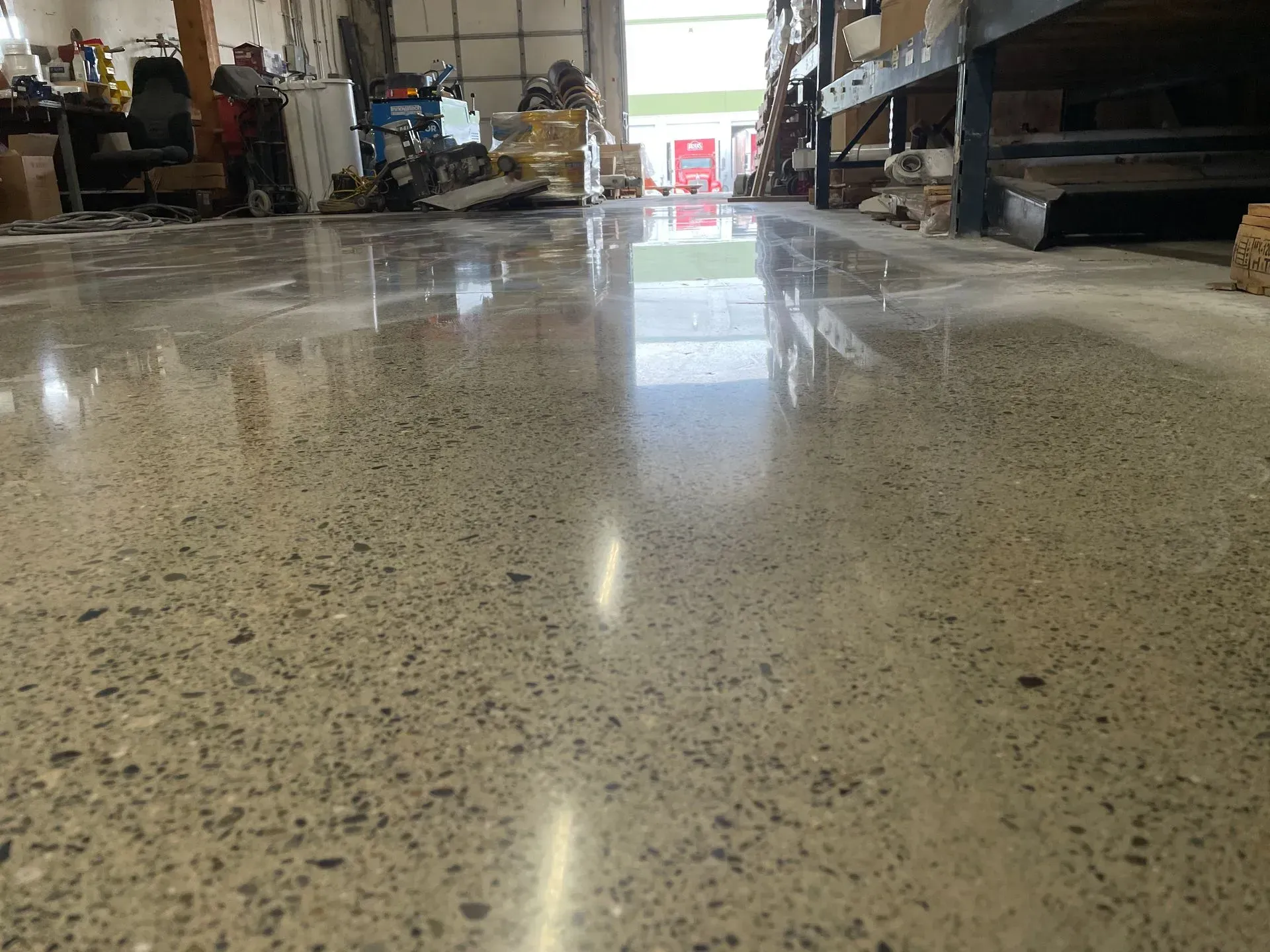 Polished concrete floor in a warehouse, reflecting overhead lights and distant objects.