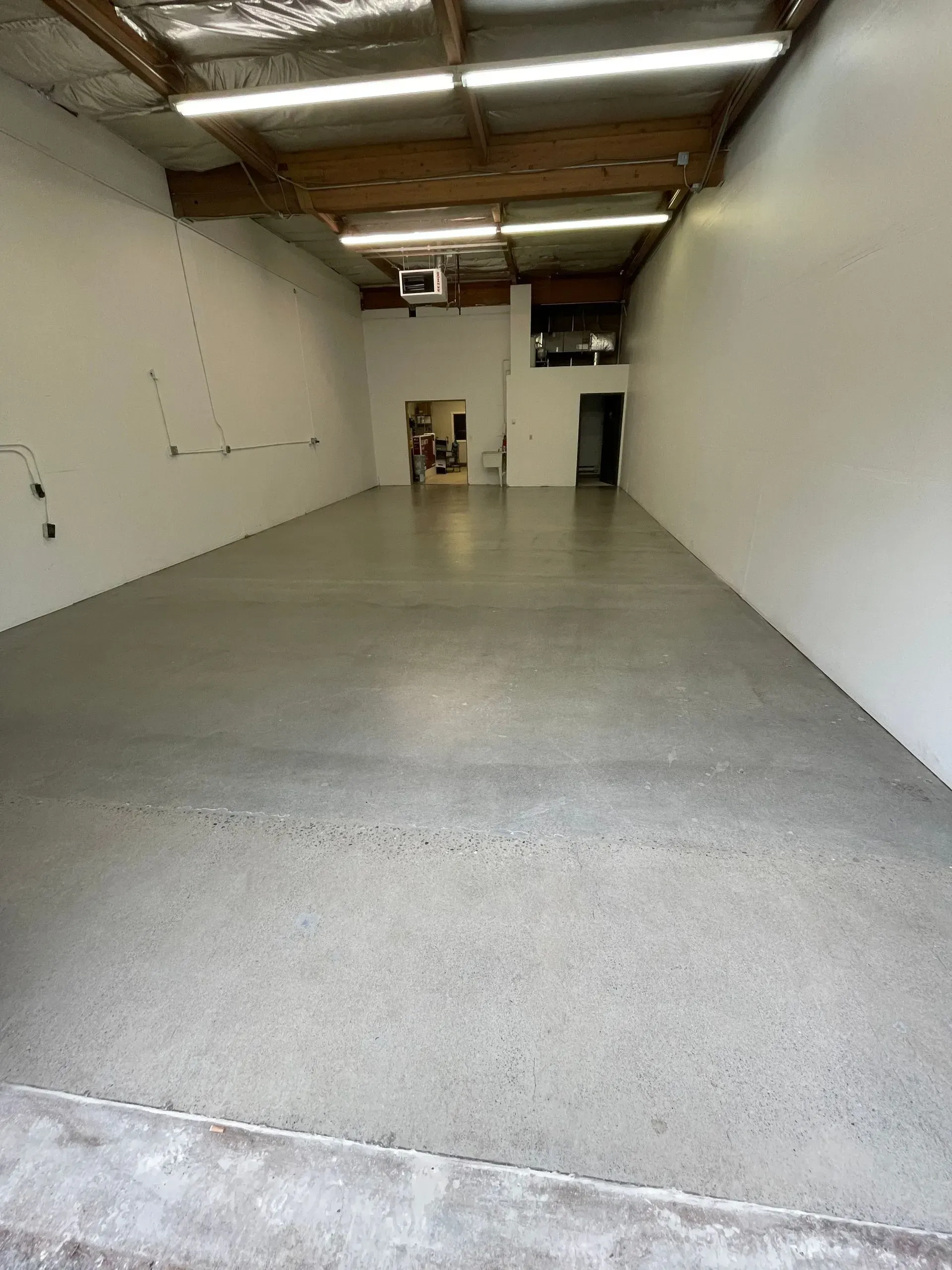 Empty commercial space with polished concrete floor, white walls, and exposed ceiling.