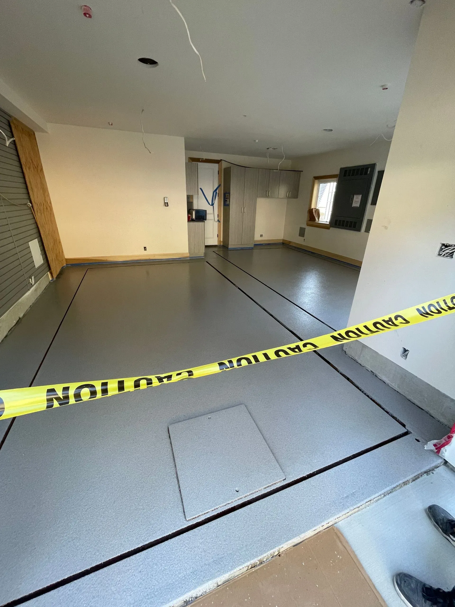 Interior view of a room under construction with gray flooring, caution tape, and unfinished walls.
