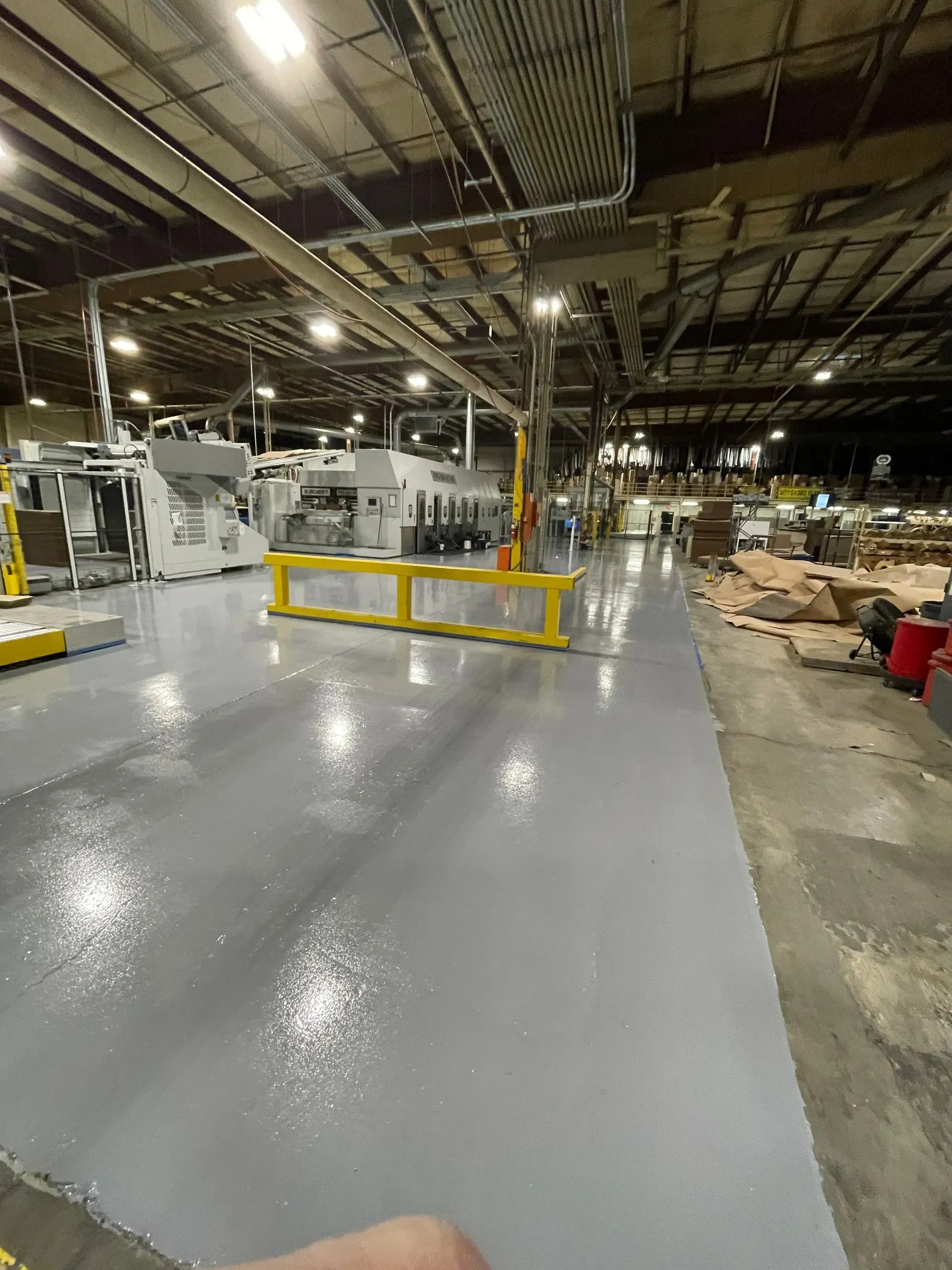 Factory floor with gray epoxy, machines, and yellow safety barriers.