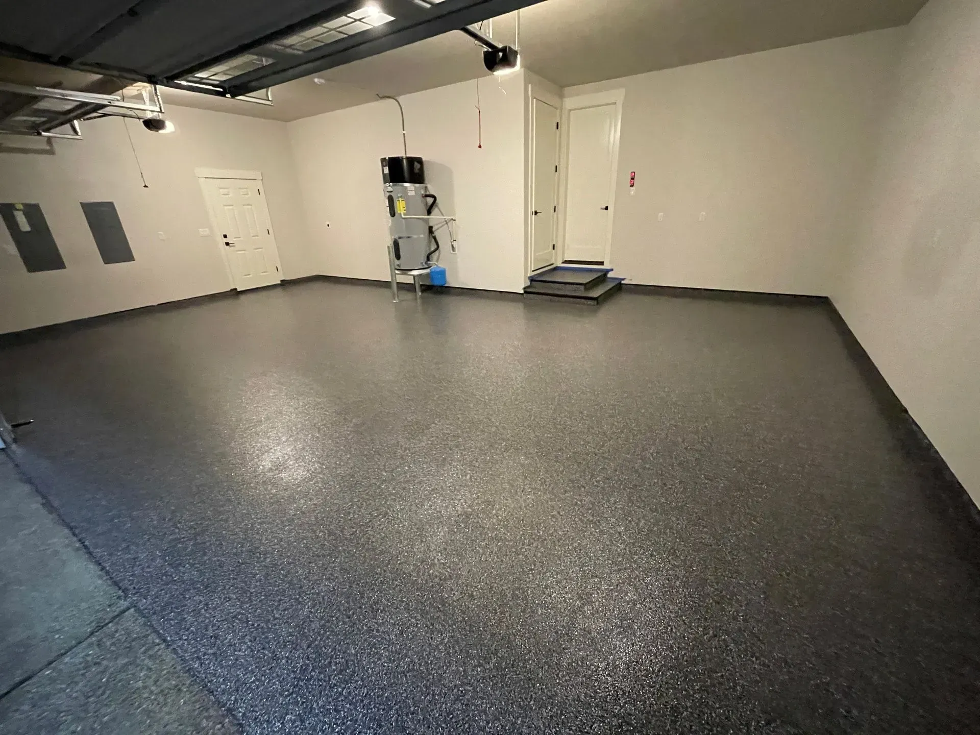 Empty garage with epoxy-coated dark gray floor, white walls, and two doors.