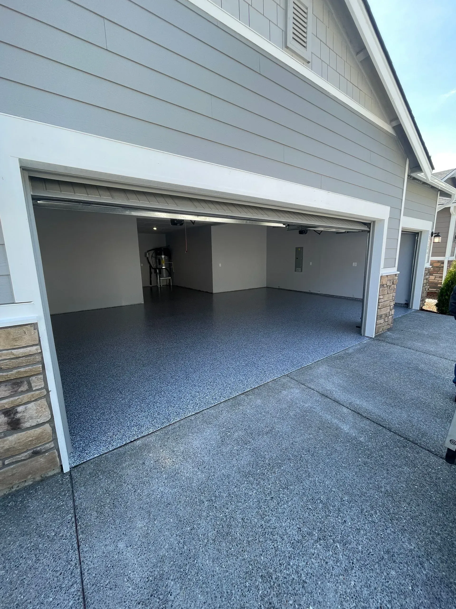 Open garage with speckled epoxy floor, gray walls, and matching exterior, on a sunny day.