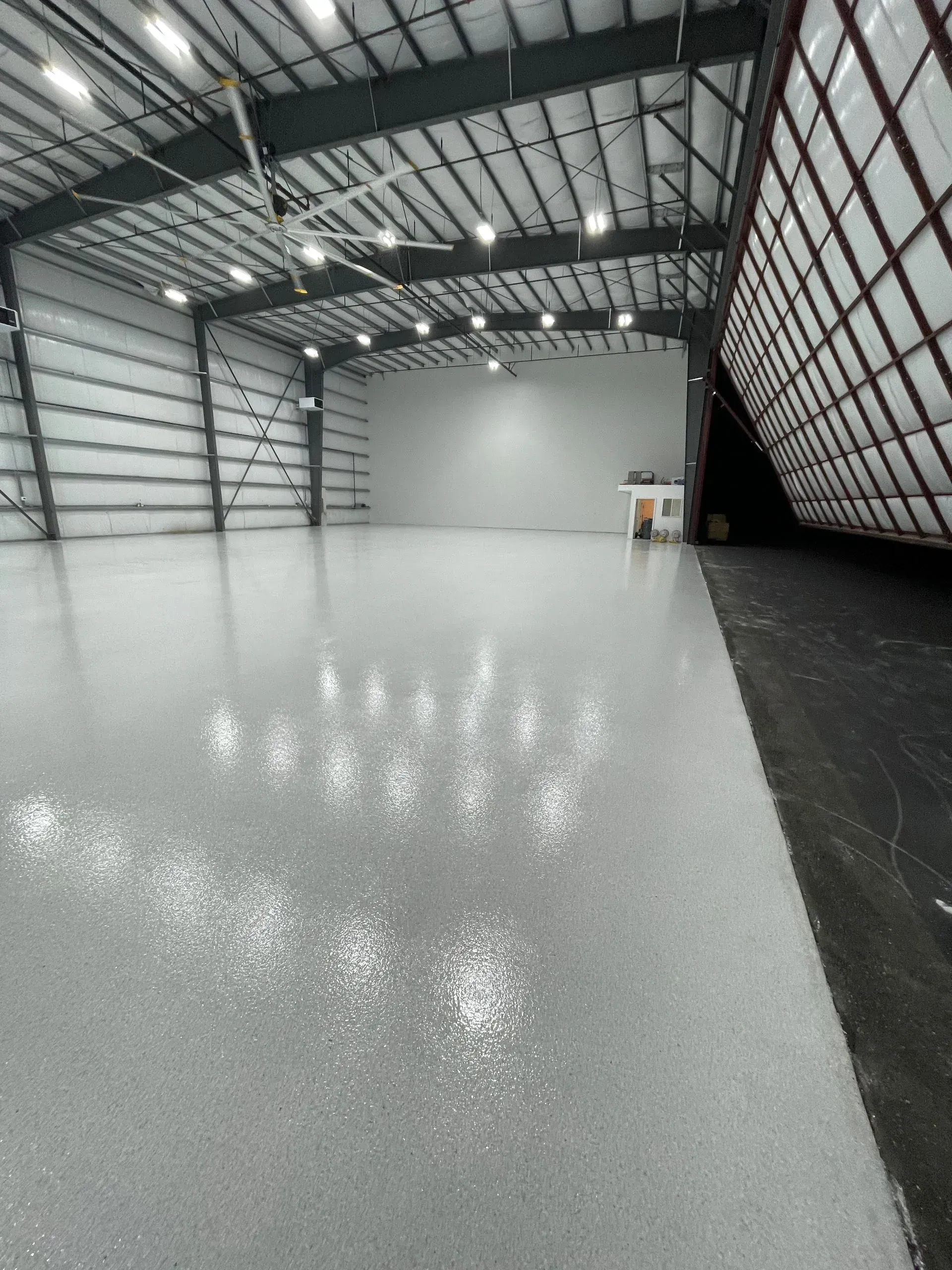 Large, empty warehouse interior with a shiny, light gray floor, metal beams, and a white back wall.