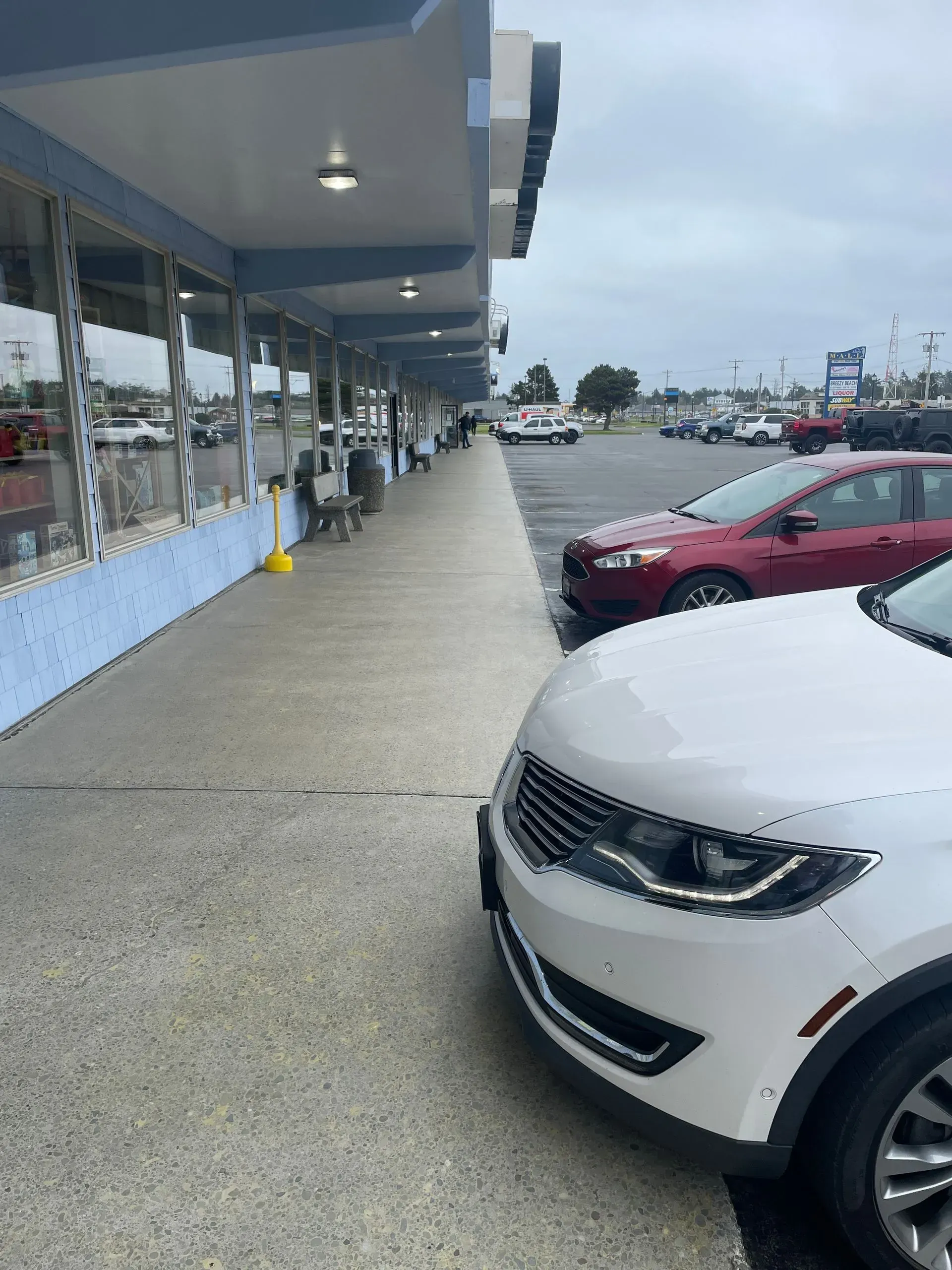 Exterior view of a building with a walkway, parked cars, and a cloudy sky.