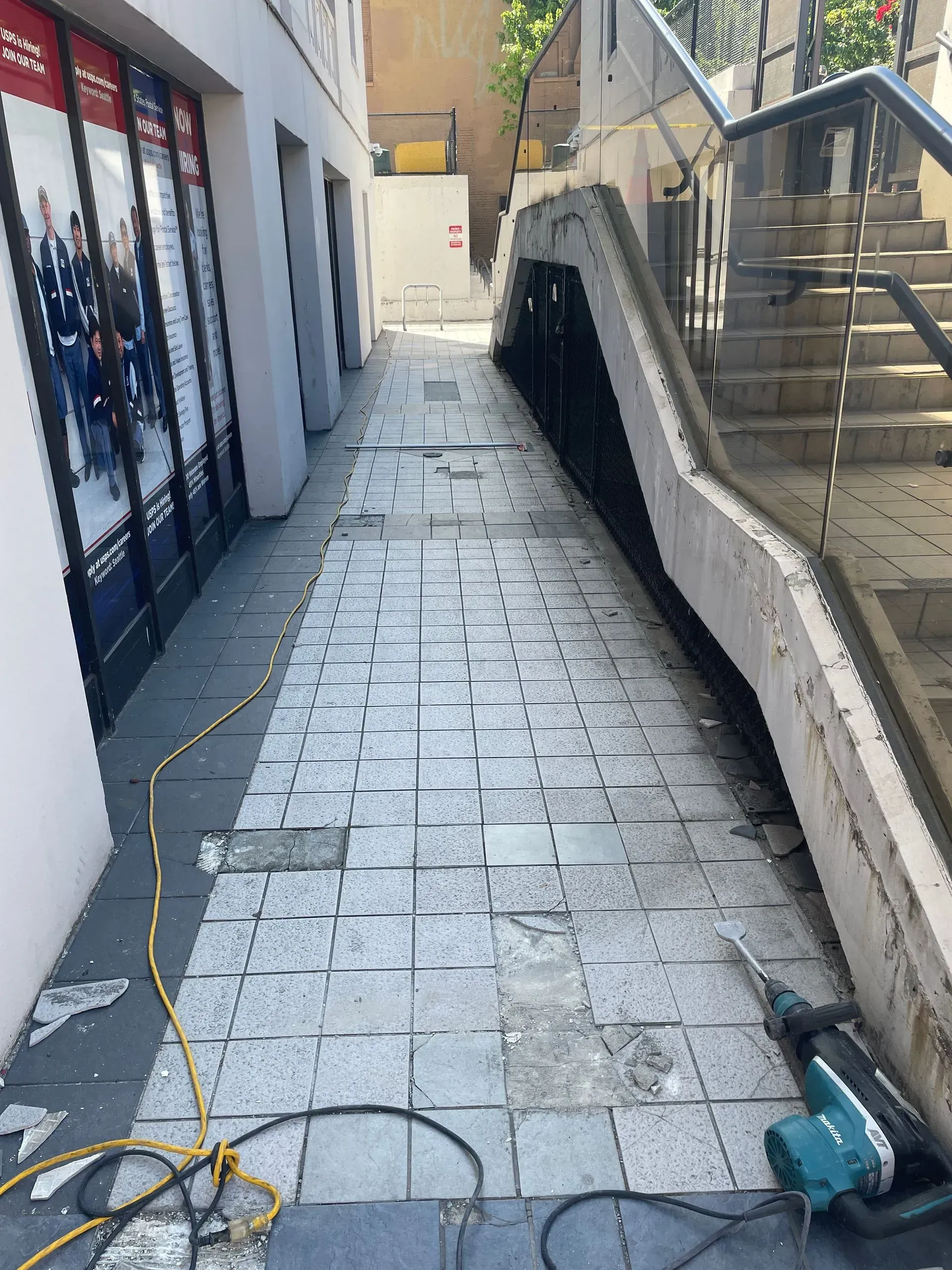 Sidewalk under construction; gray stone tiles with sections removed. Staircase on right, storefront on left.