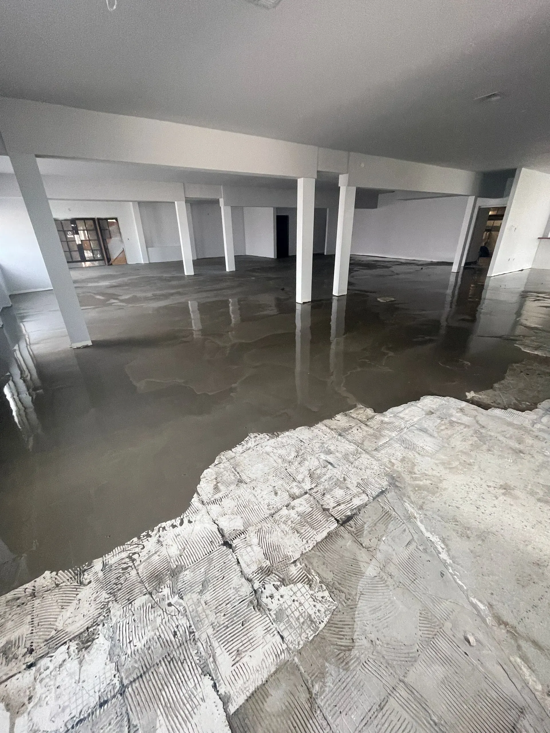 Interior view of a large, empty room with concrete flooring and support columns.