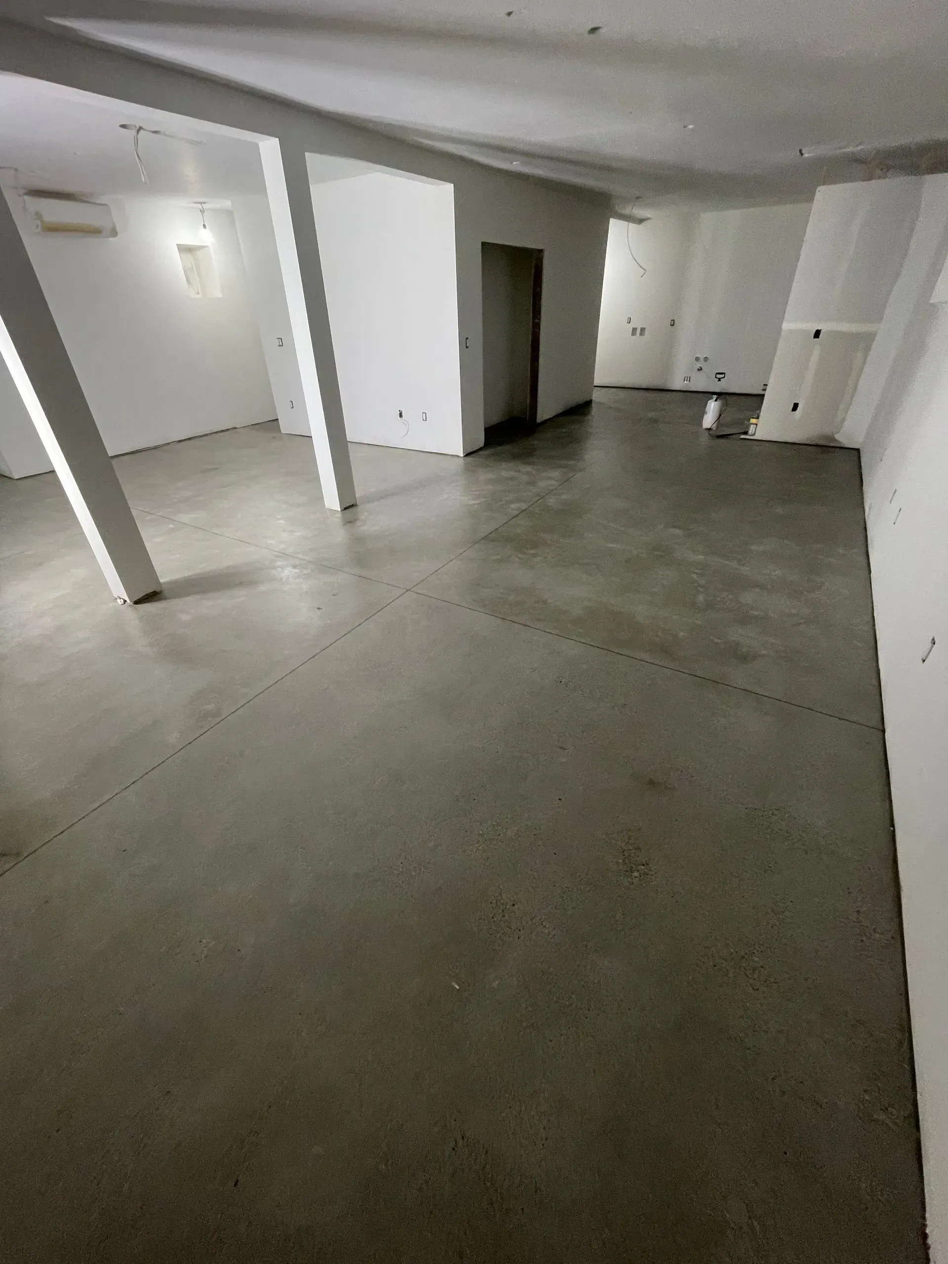 Empty room with concrete floor, white walls, support pillars, and doorway.
