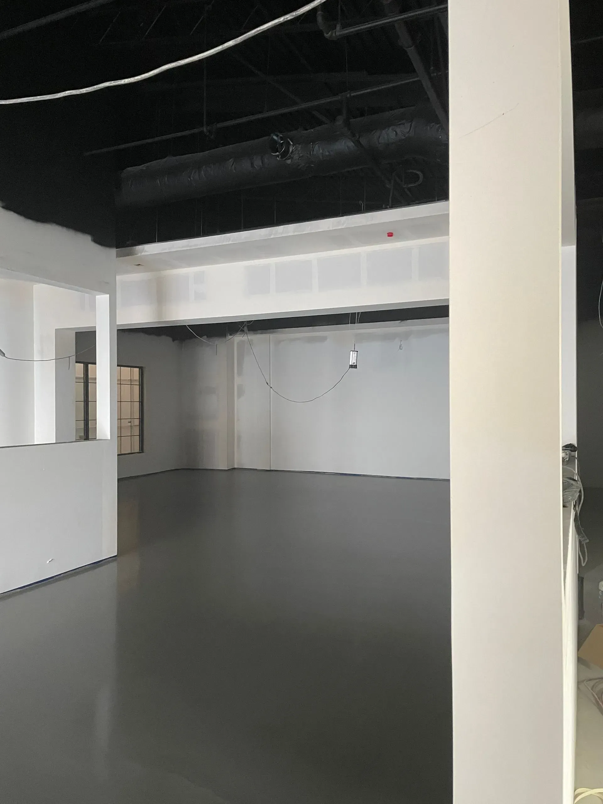 Empty commercial space with gray floors, white walls, and a black ceiling.