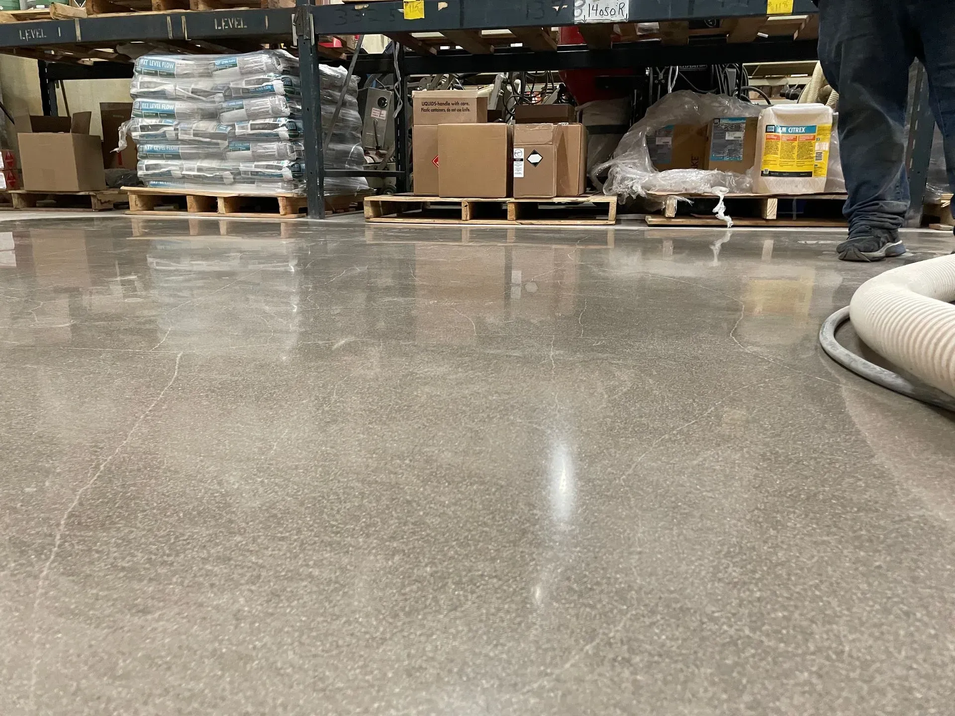 Polished concrete floor in a warehouse, with shelving, pallets, and a person's legs visible.