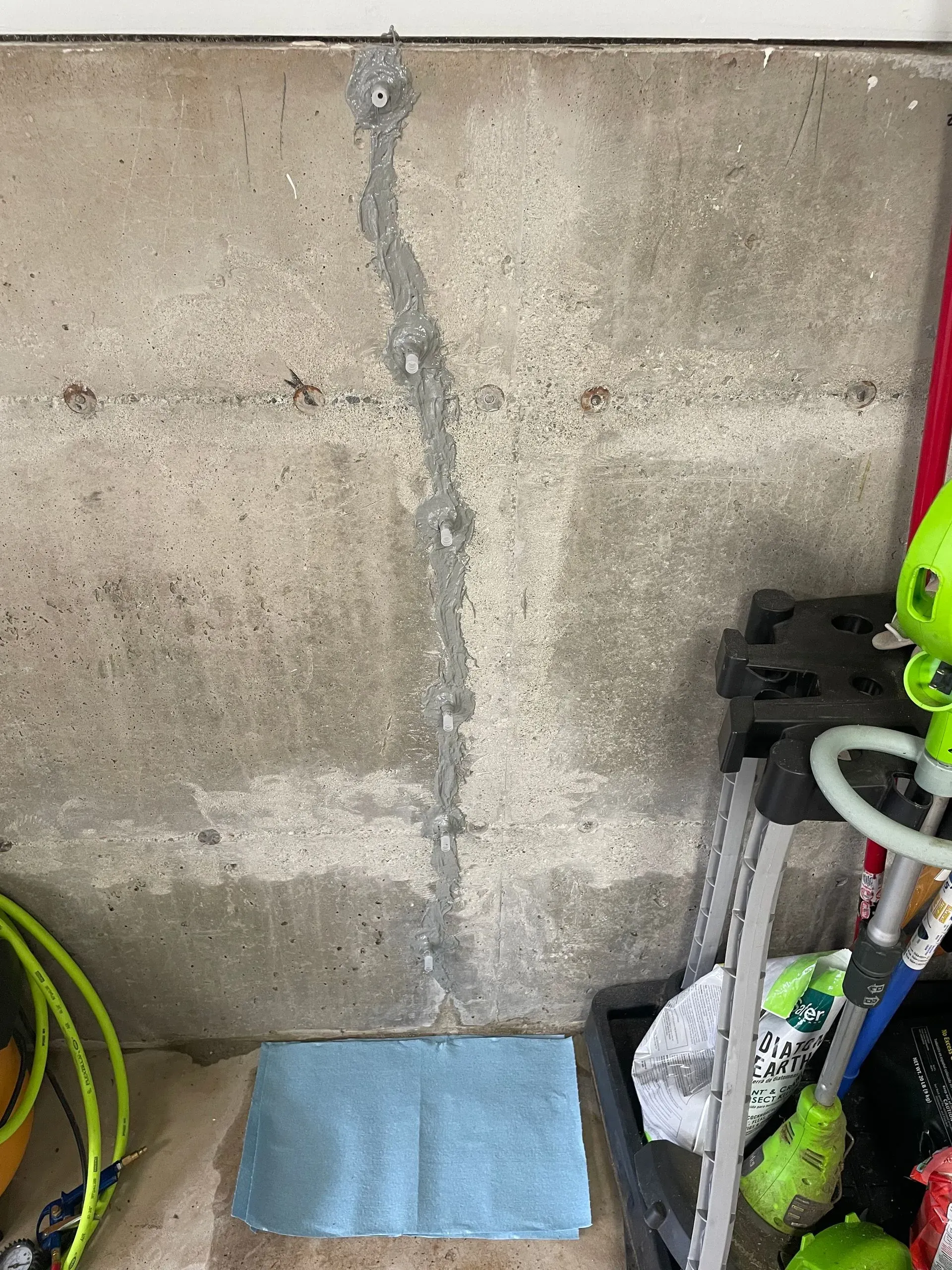 Concrete wall with vertical crack, patched in gray, near a step stool and tools.