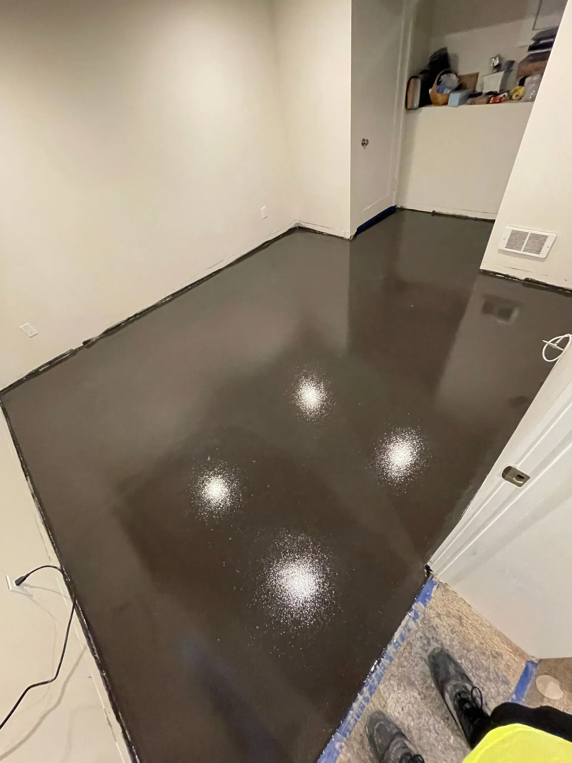 Dark brown, glossy floor in a room. White walls. Four bright spots on the floor.