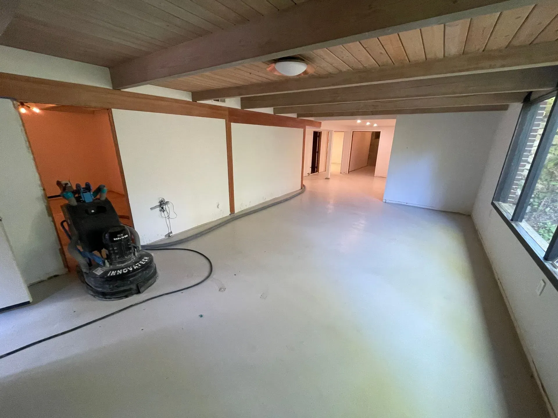 Interior view of a room with exposed beams and a floor polisher. Walls are white and orange.