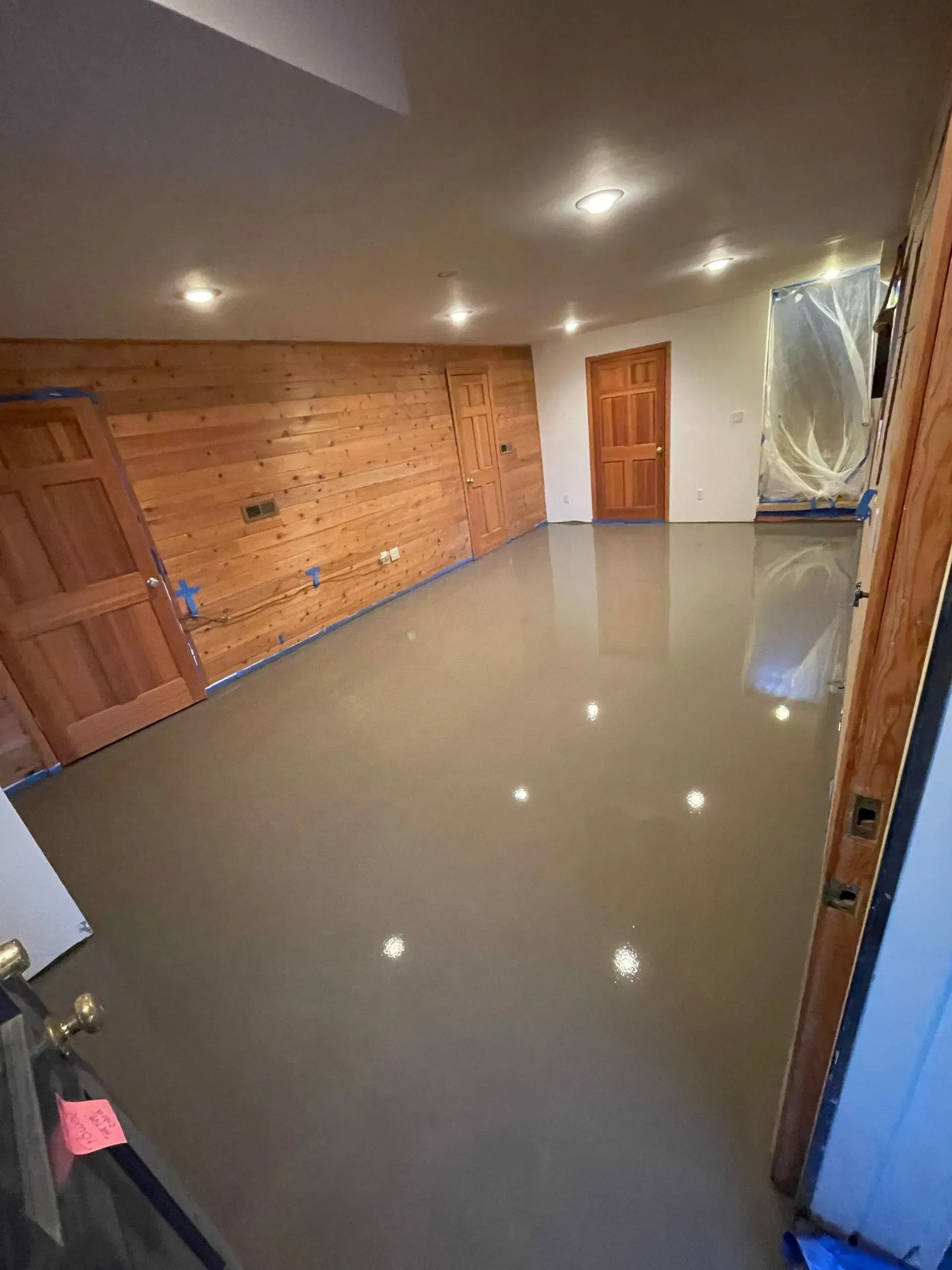 Empty room with polished gray floor, wood paneling on one wall, and wooden doors.