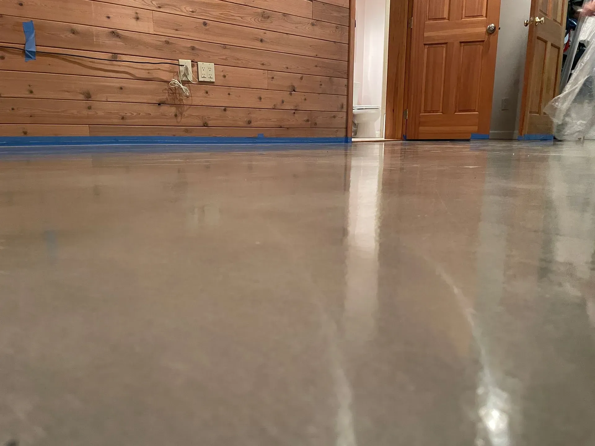 Shiny gray concrete floor reflecting light; wood-paneled wall, open door in background.