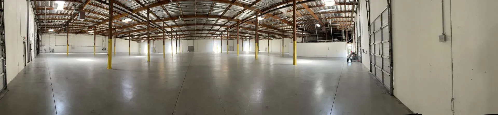 Interior of a large, empty warehouse with concrete floor, wooden beams, and support pillars.