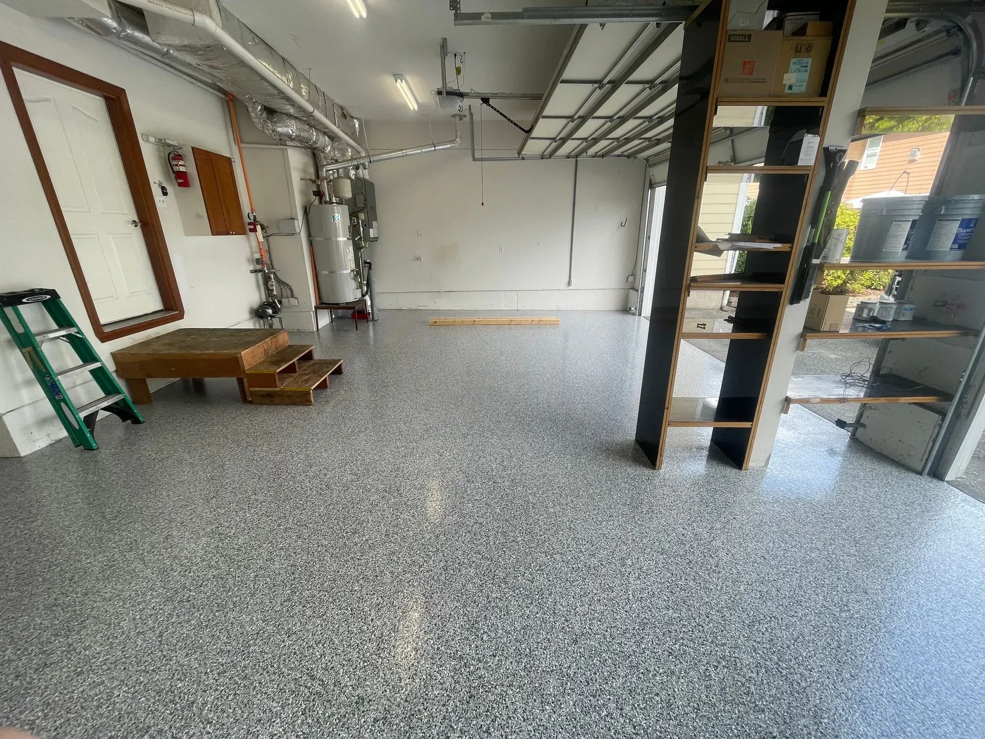 Garage with gray speckled epoxy floor, tools, and shelves. Garage door is open.