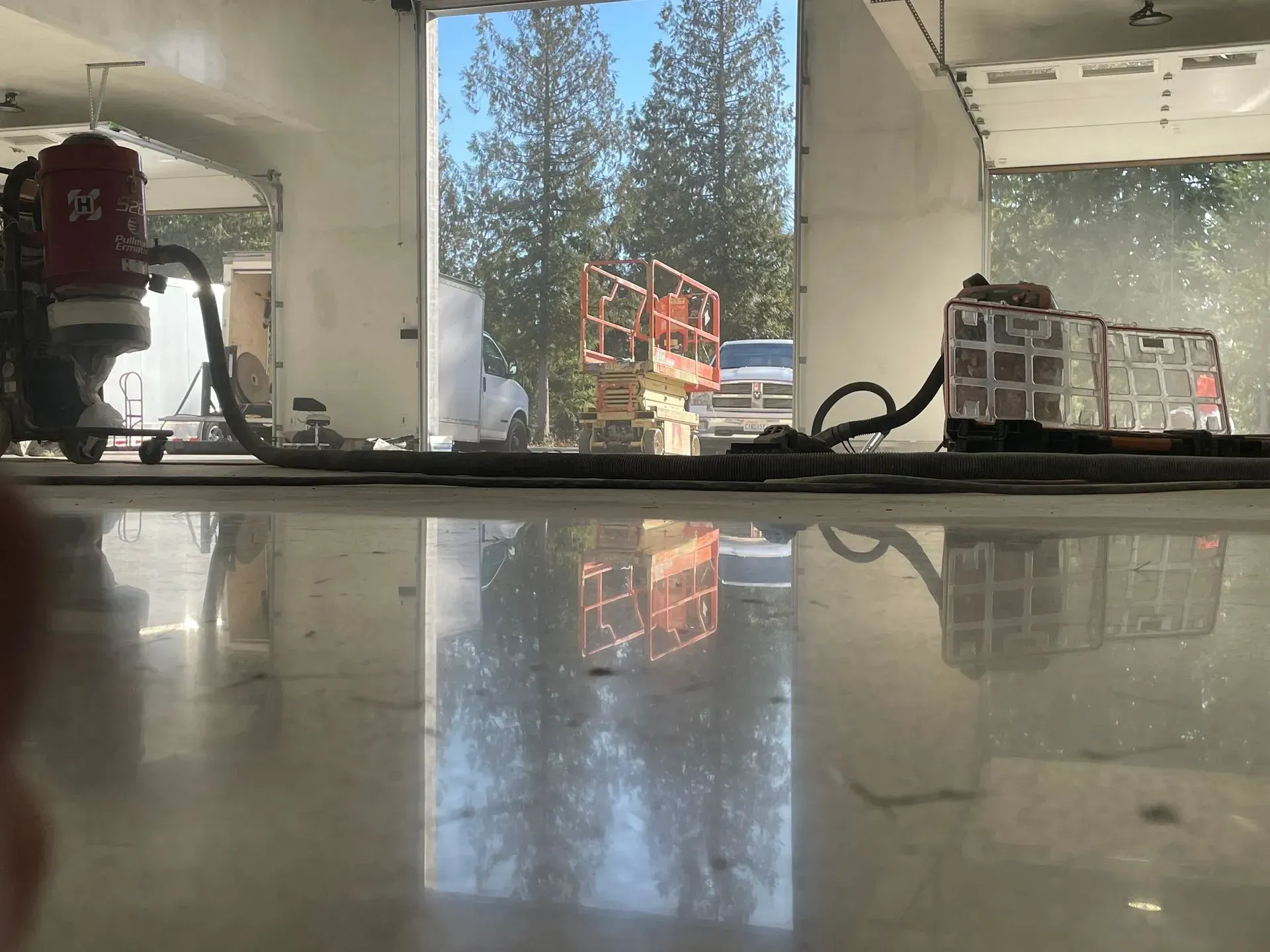 Shiny concrete floor reflecting outside through open garage door. Construction equipment inside.