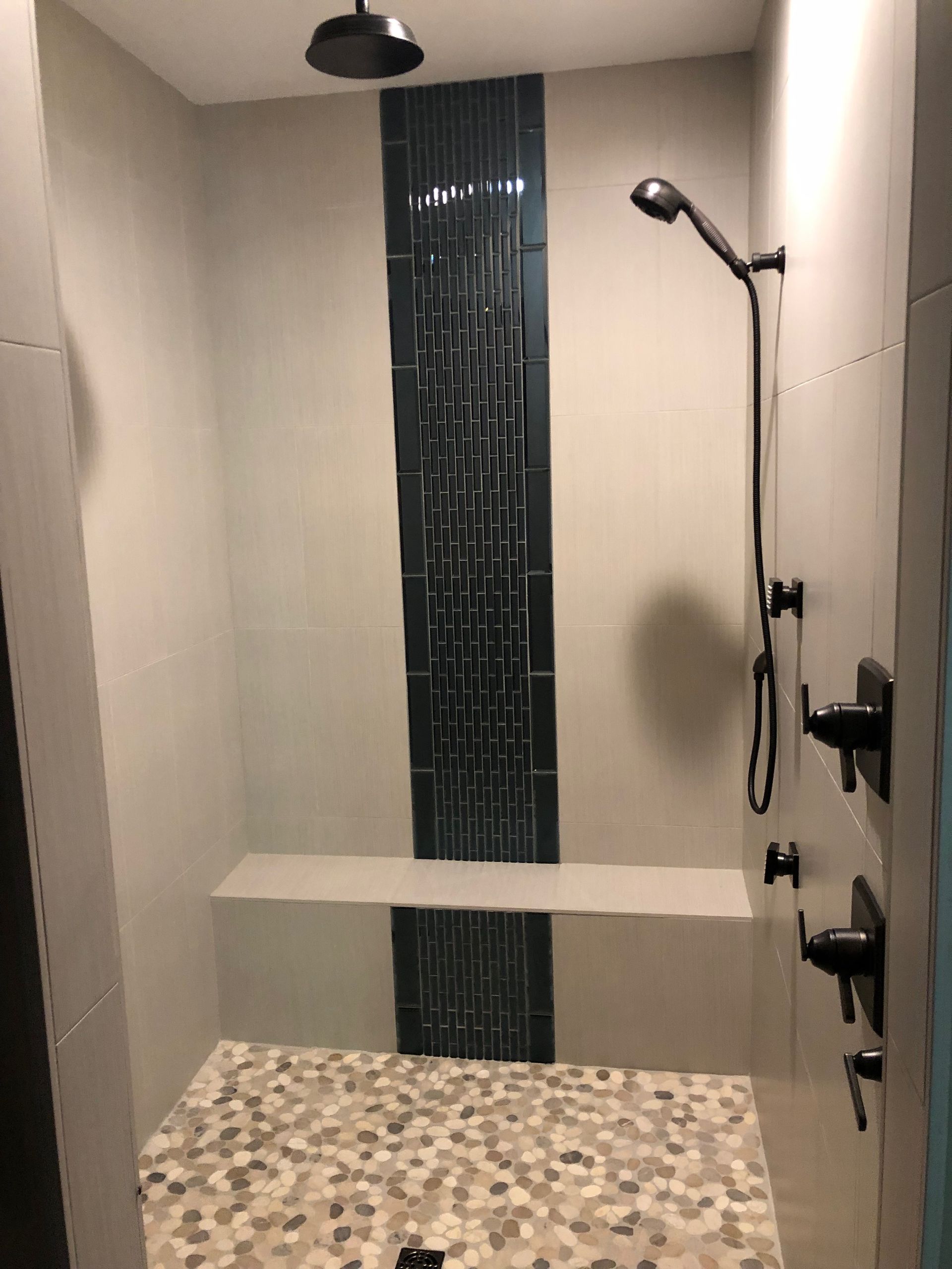 Modern shower with dark blue accent tile, pebble floor, built-in bench, and black fixtures.