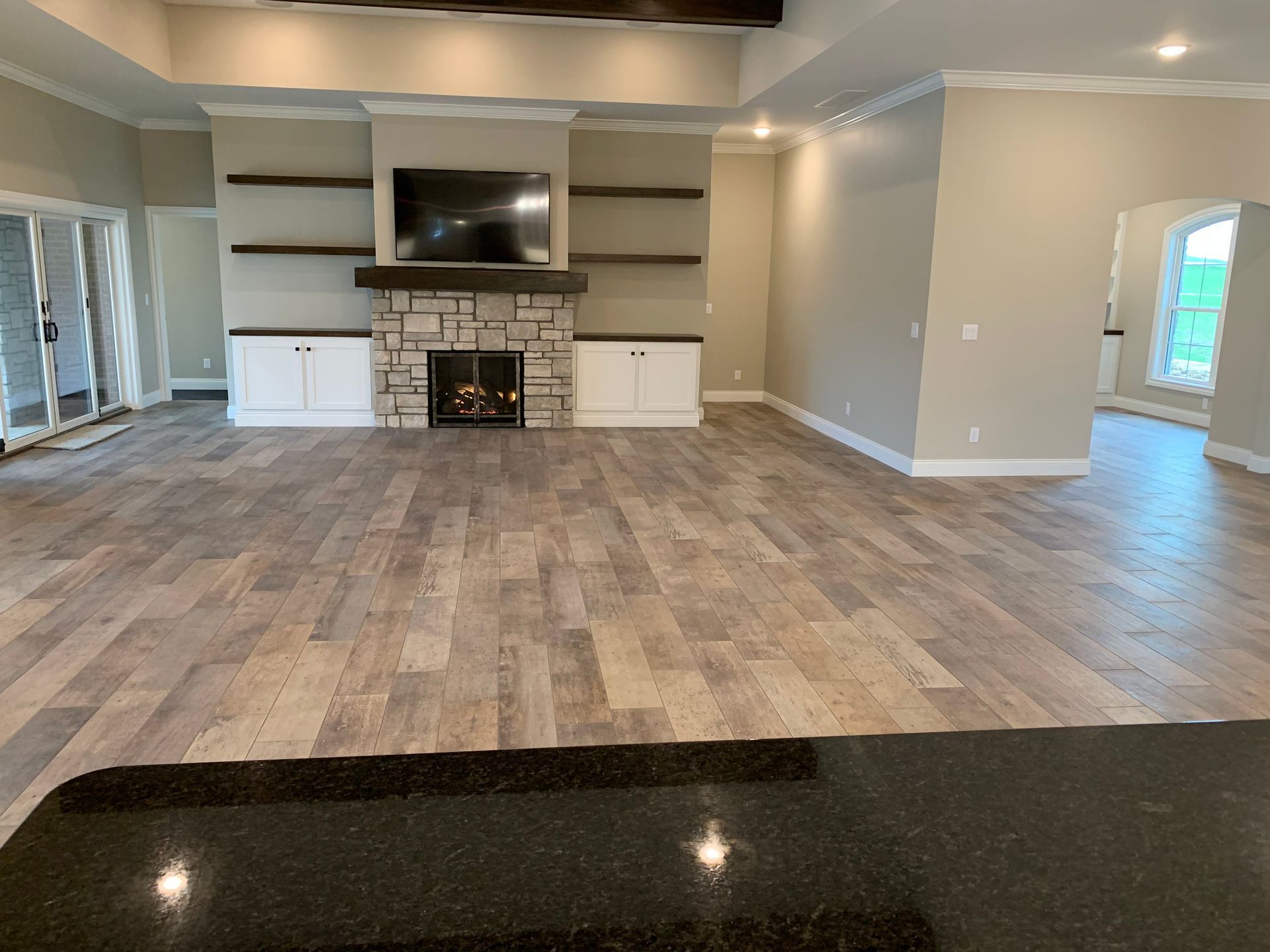 Spacious living room with stone fireplace, built-in shelves, wood-look floor, and neutral walls.