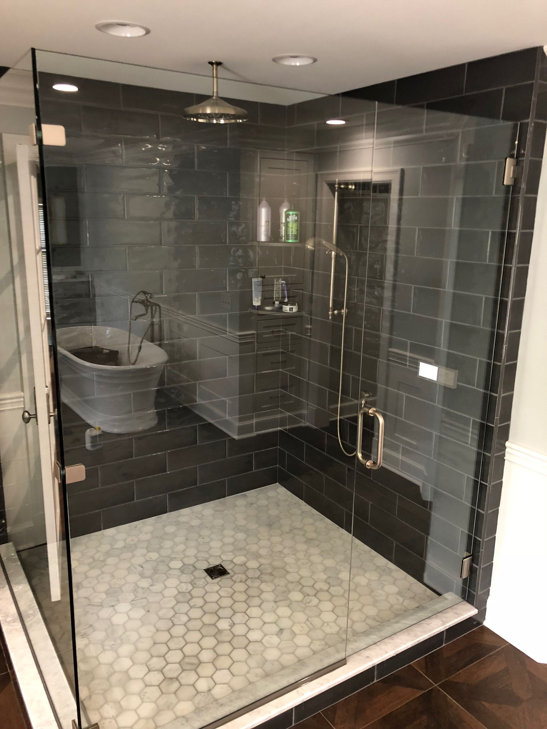 Modern bathroom with a glass shower, dark tile walls, and a metal tub.