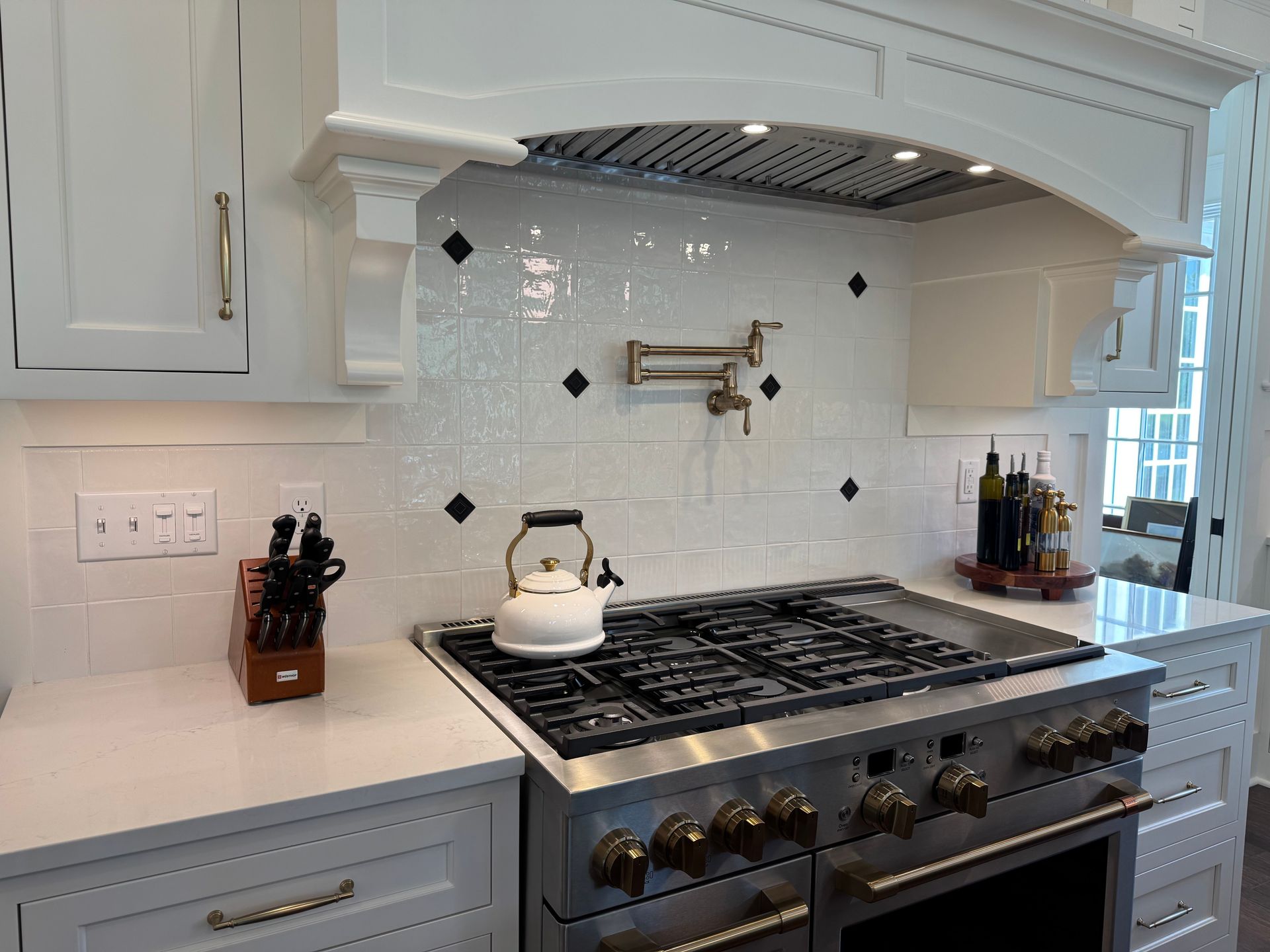 White kitchen with stainless steel stove, white cabinets, and white backsplash.