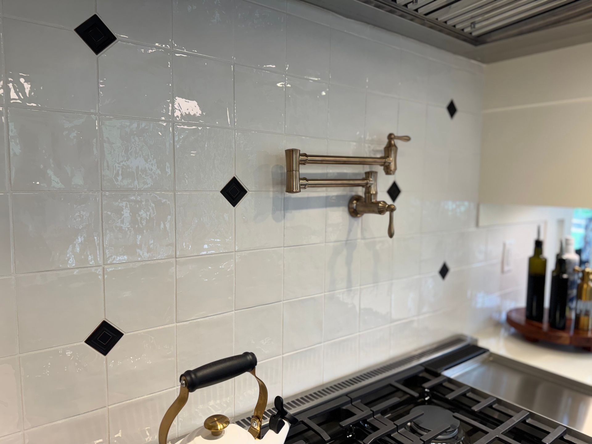 White tiled kitchen backsplash with black diamond accents and a pot filler faucet above a gas range.