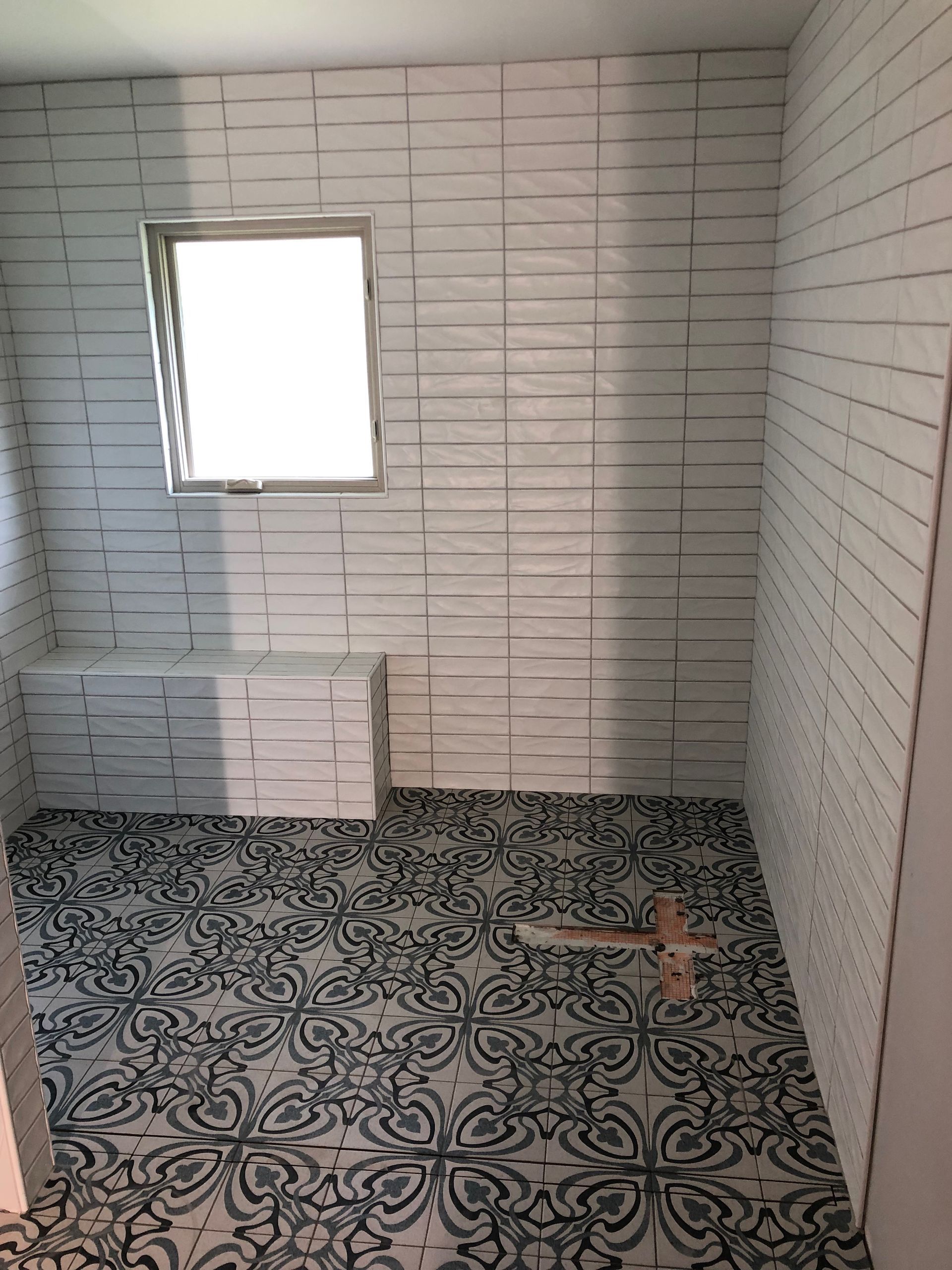 Bathroom with white textured wall tiles, patterned floor tiles, and a small window.