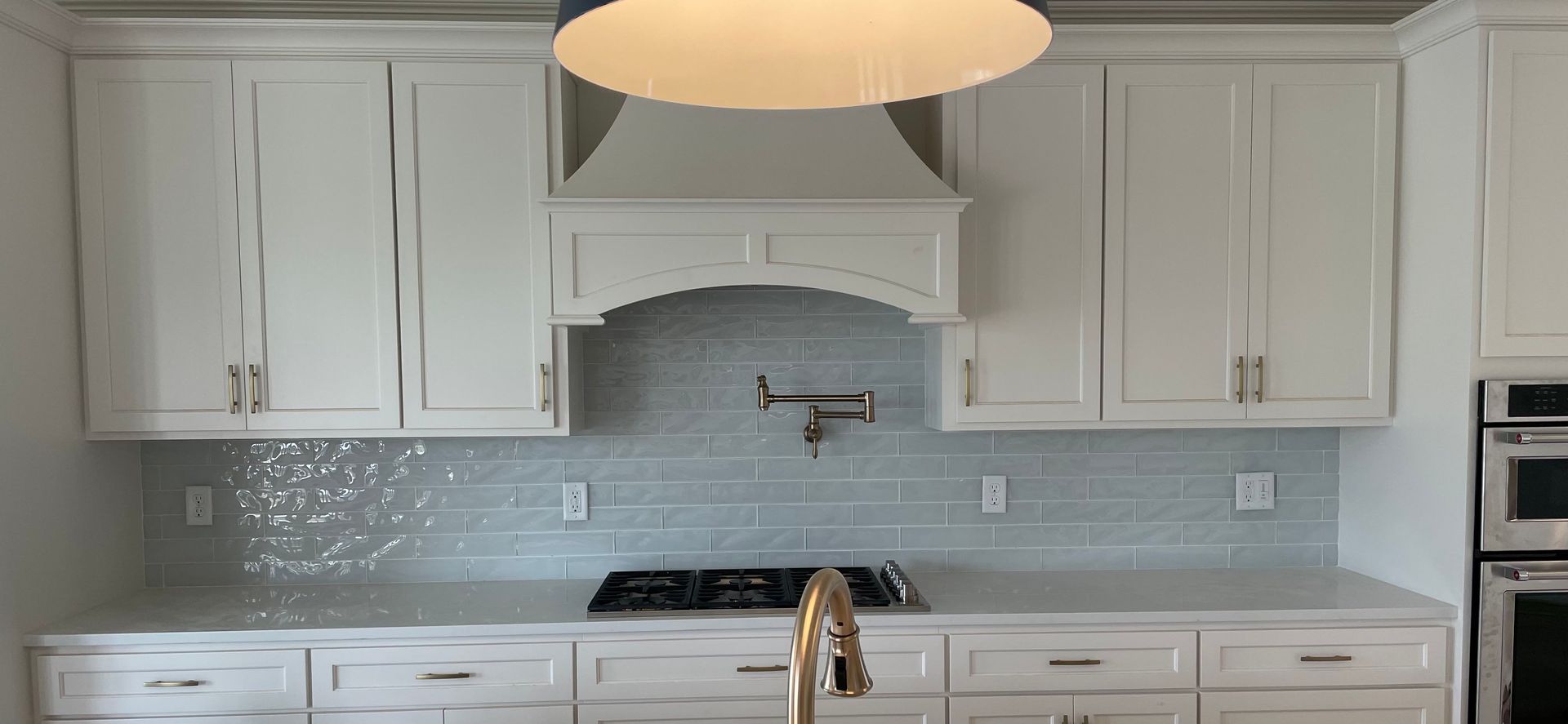 White kitchen with light blue backsplash, stove, sink, and cabinets.