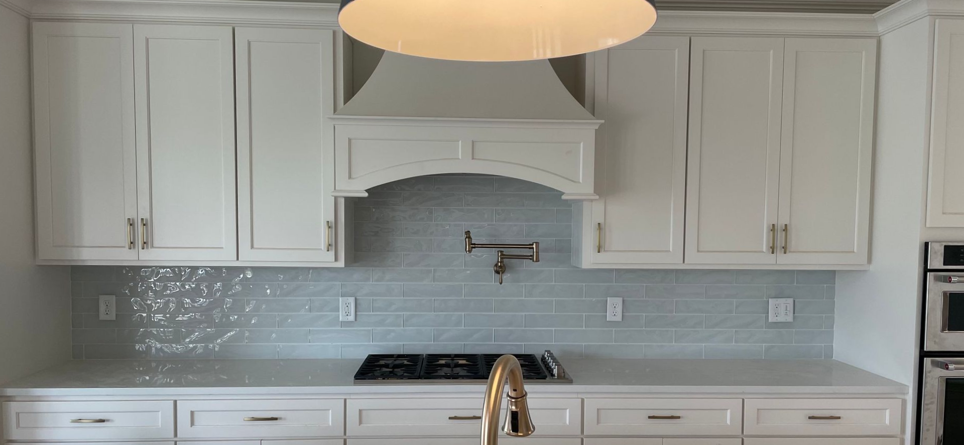 White kitchen with light blue backsplash, stove, sink, and cabinets.