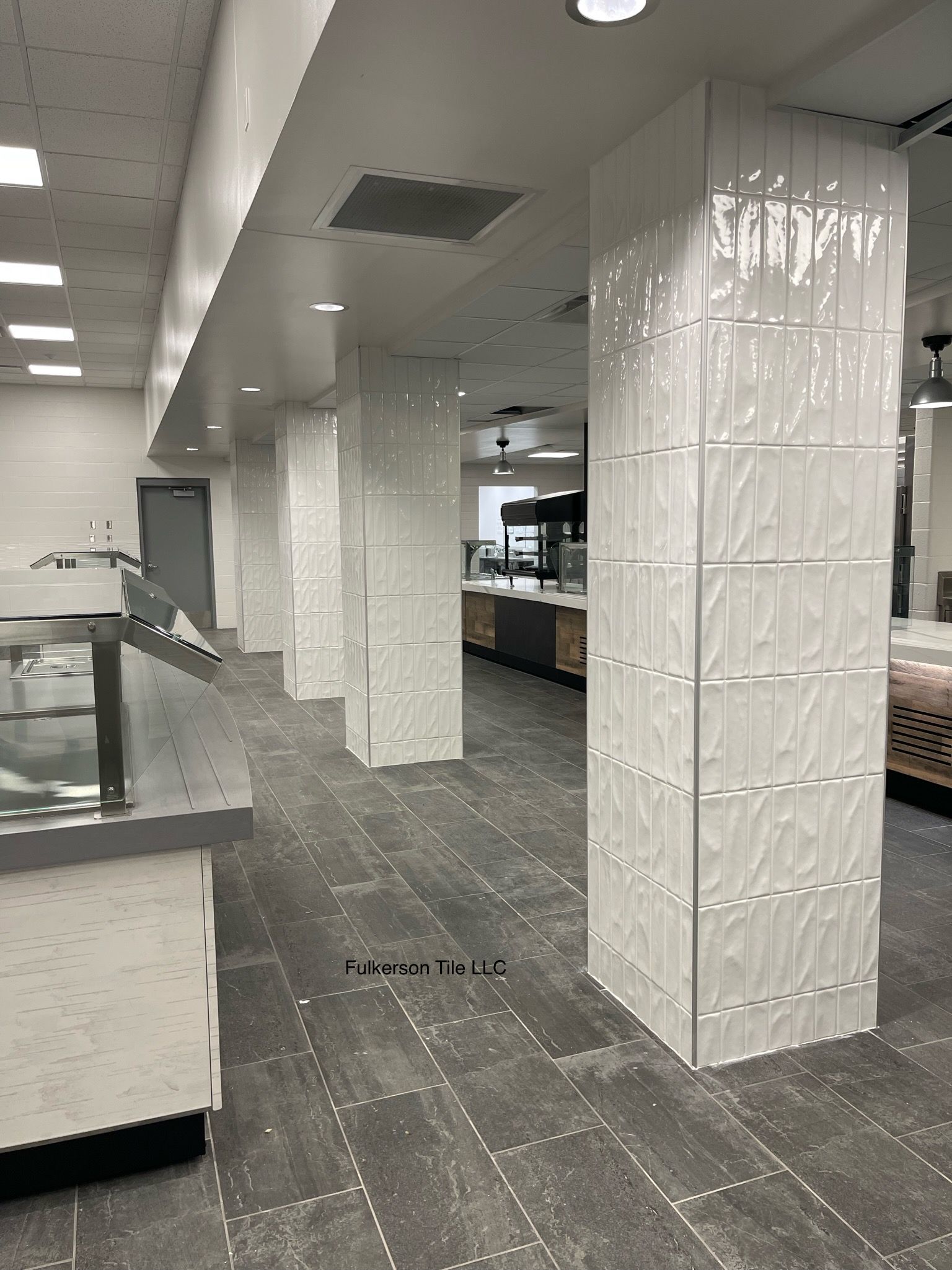 Interior with white textured columns, gray floor, and kitchen in the distance.