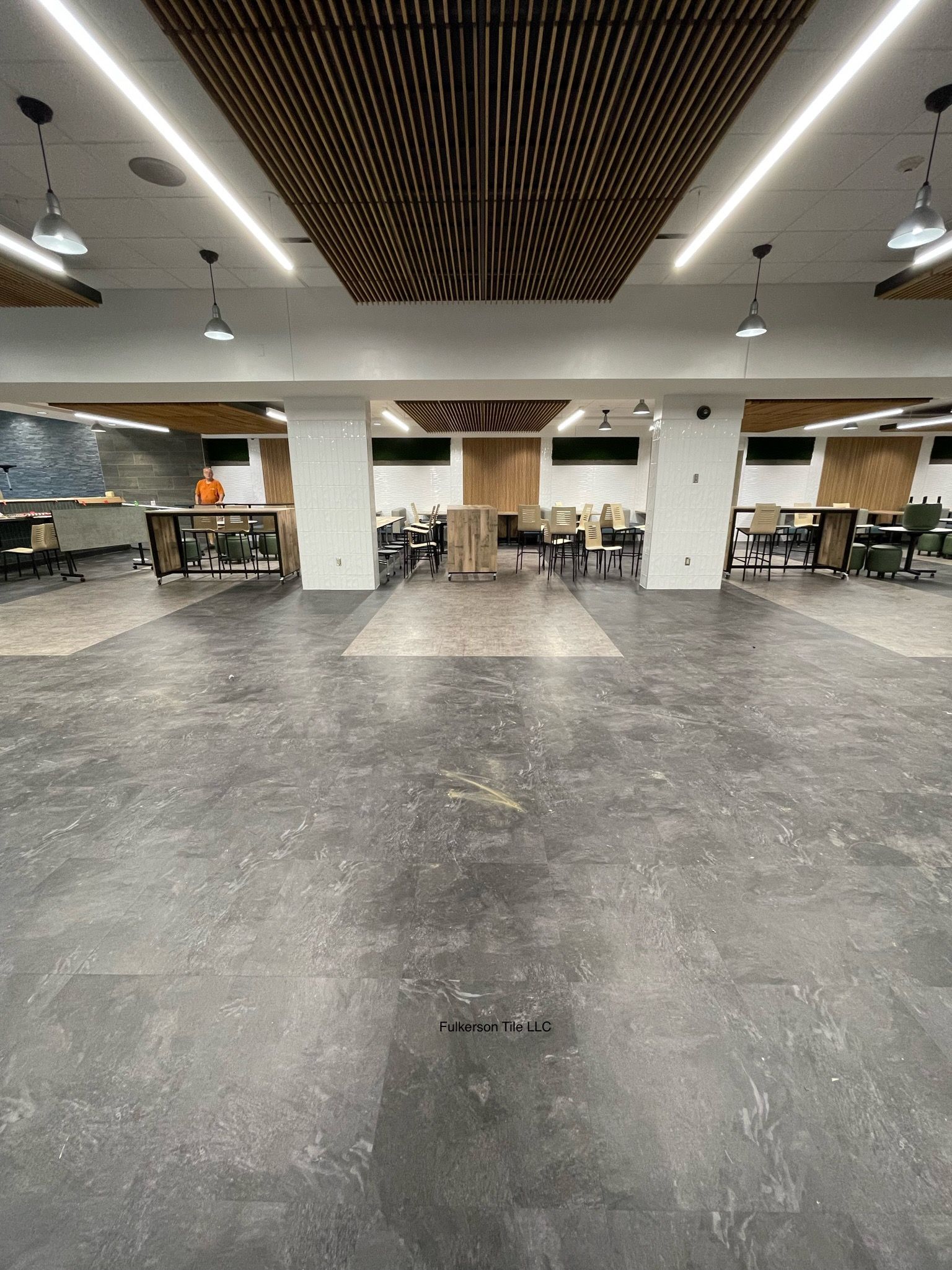 Wide, empty room with concrete floor, acoustic ceiling panels, and support columns.
