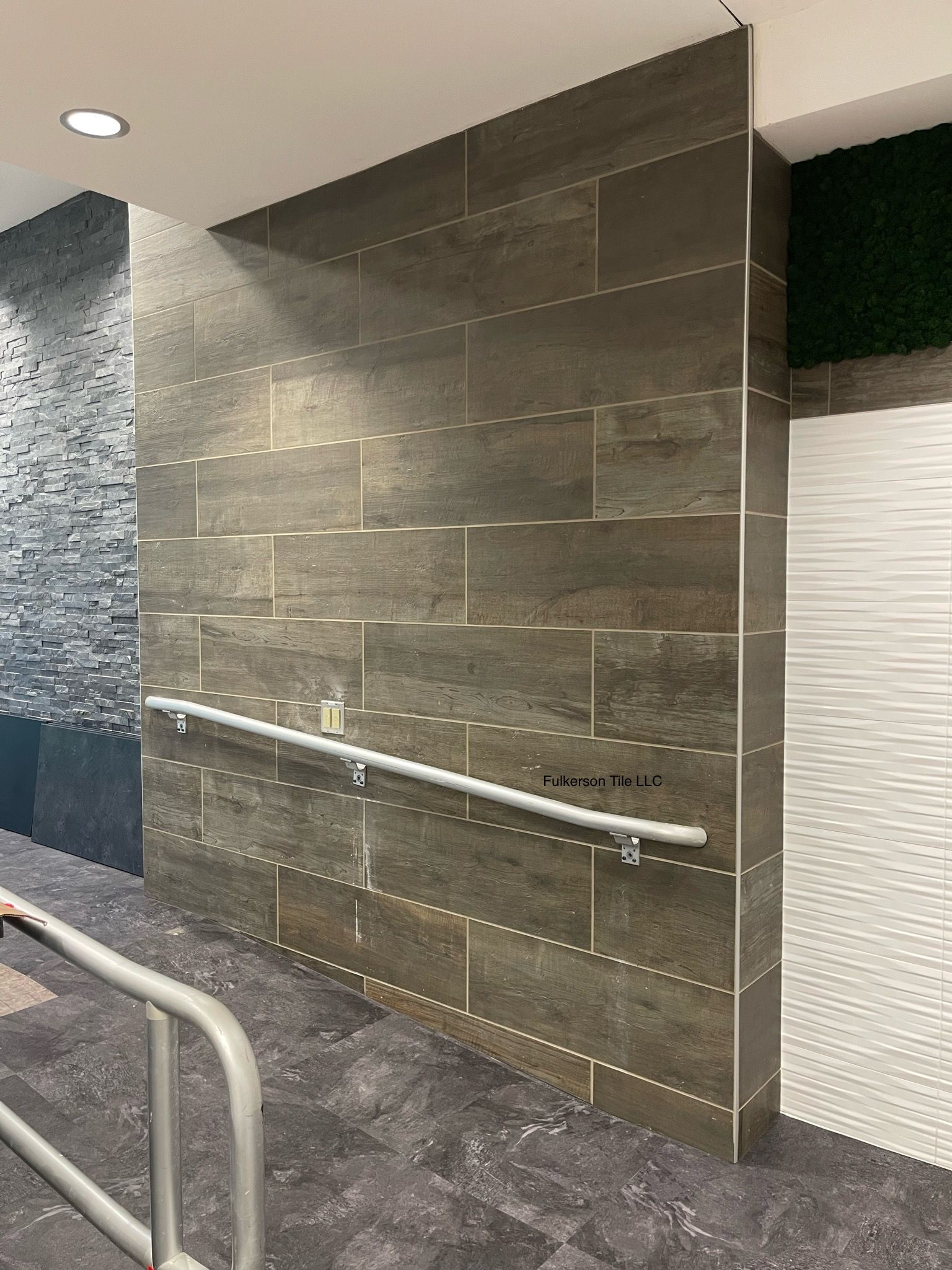 Gray tiled wall with handrail, entrance to right, with textured wall on left.