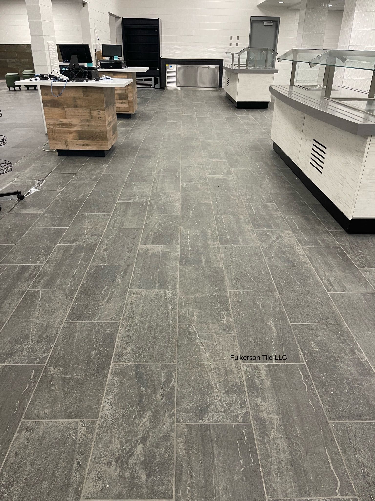 Empty commercial space with gray tiled floor, display counters, and stainless steel appliances.