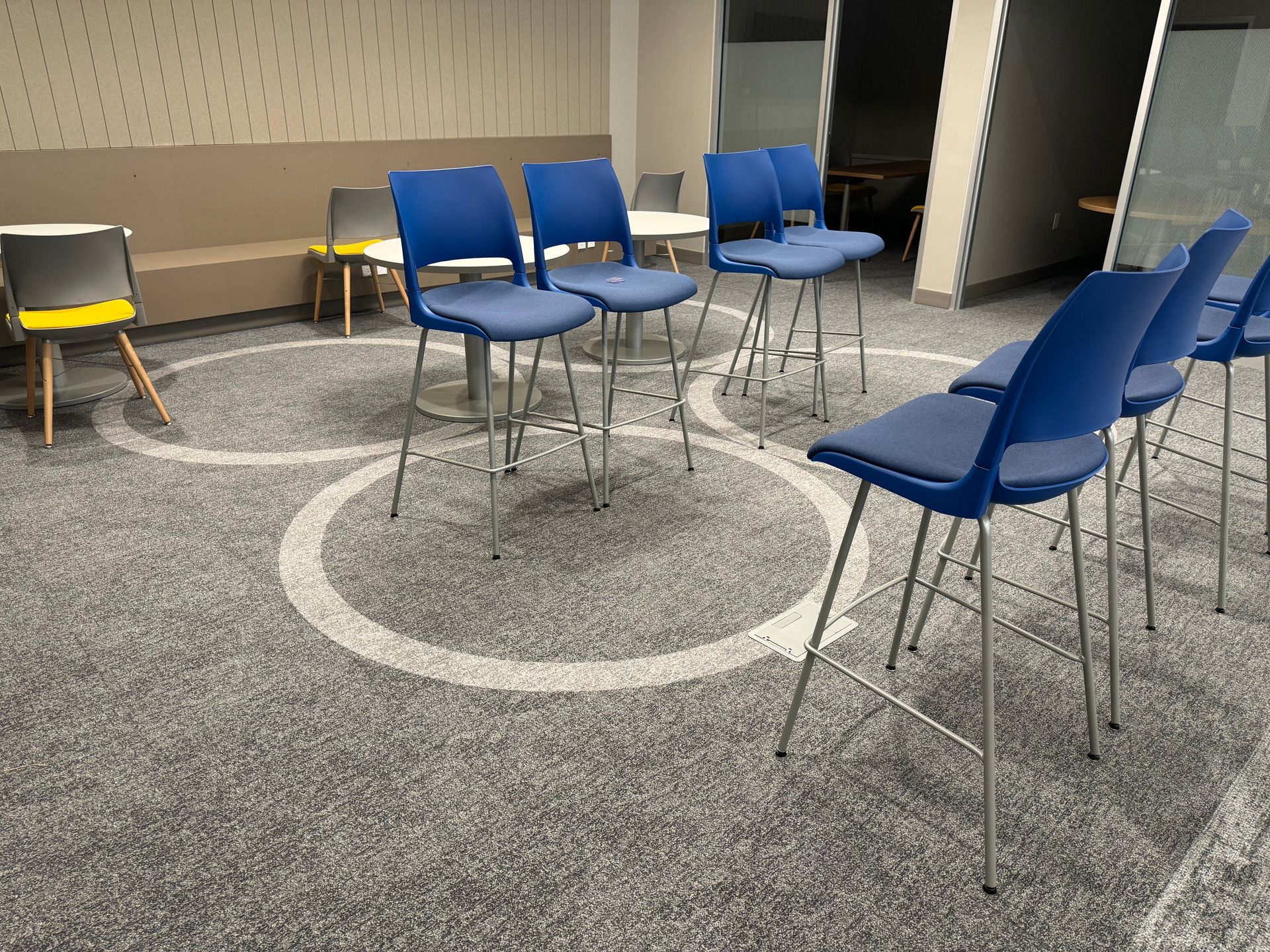 Room with blue chairs arranged in a circle, white circles on the carpet.