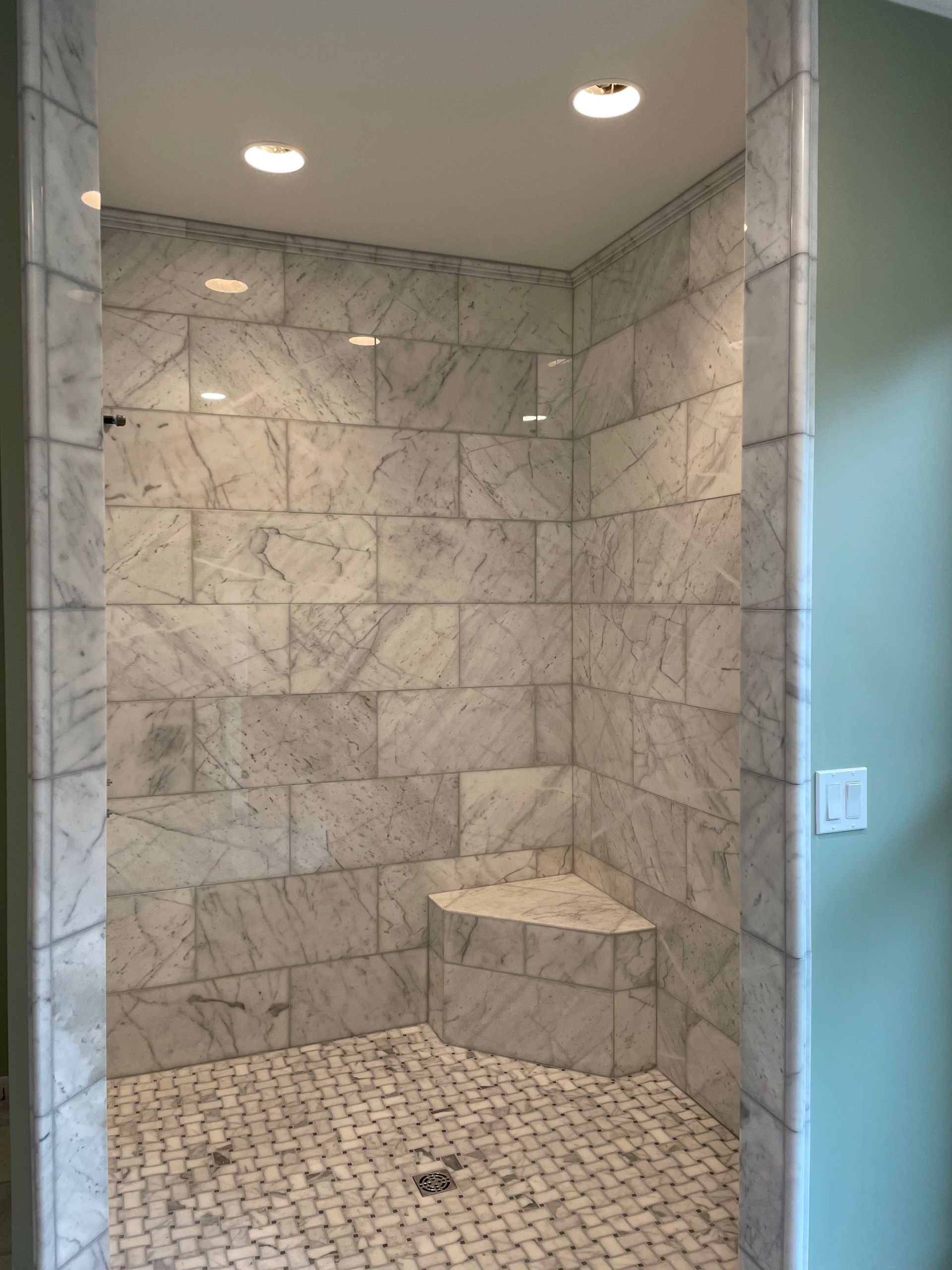 Marble-tiled shower with built-in bench, three recessed lights, and small mosaic floor tiles.