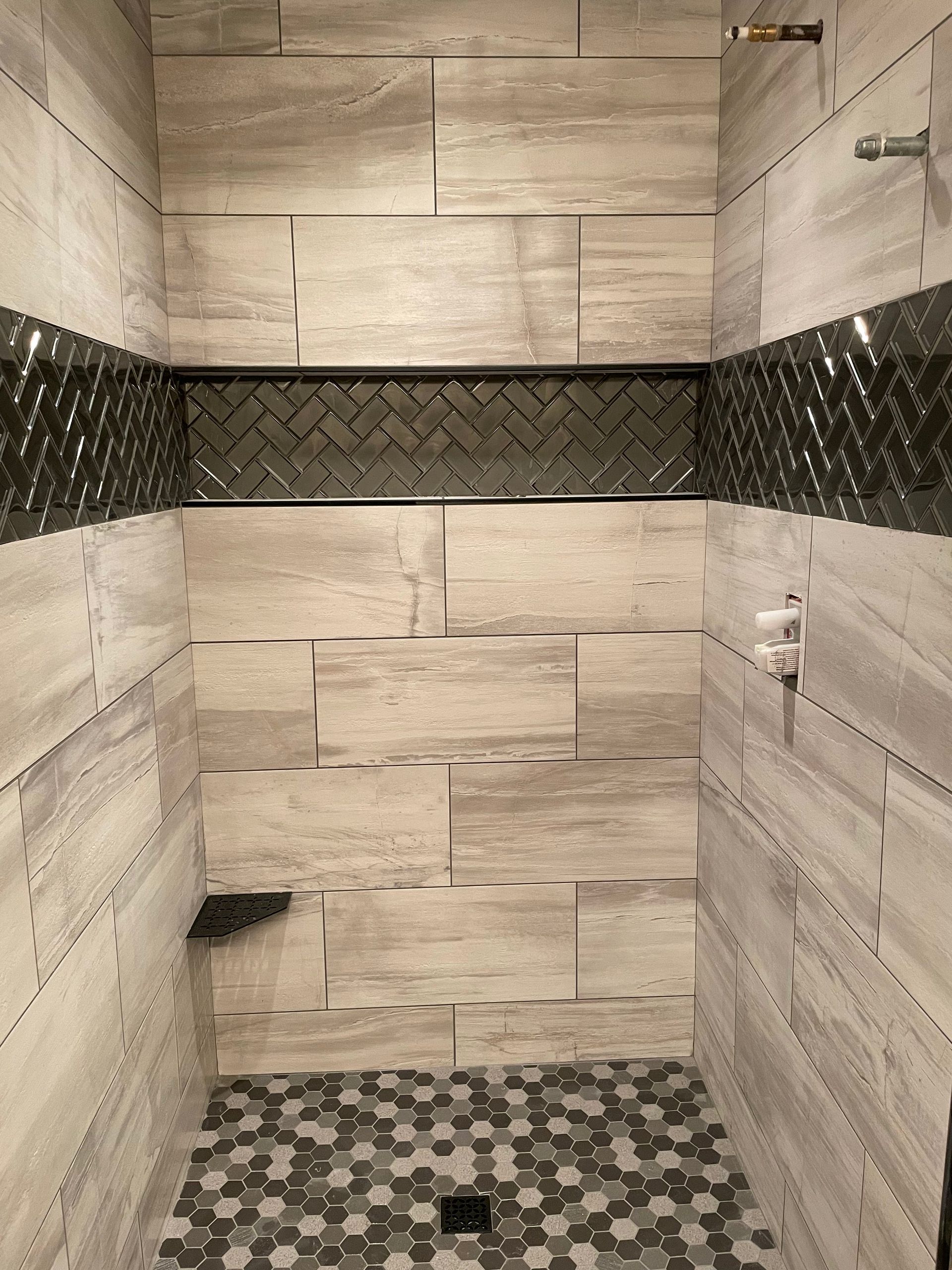 Shower stall with light brown rectangular tiles, a dark accent strip, and a pebble floor.
