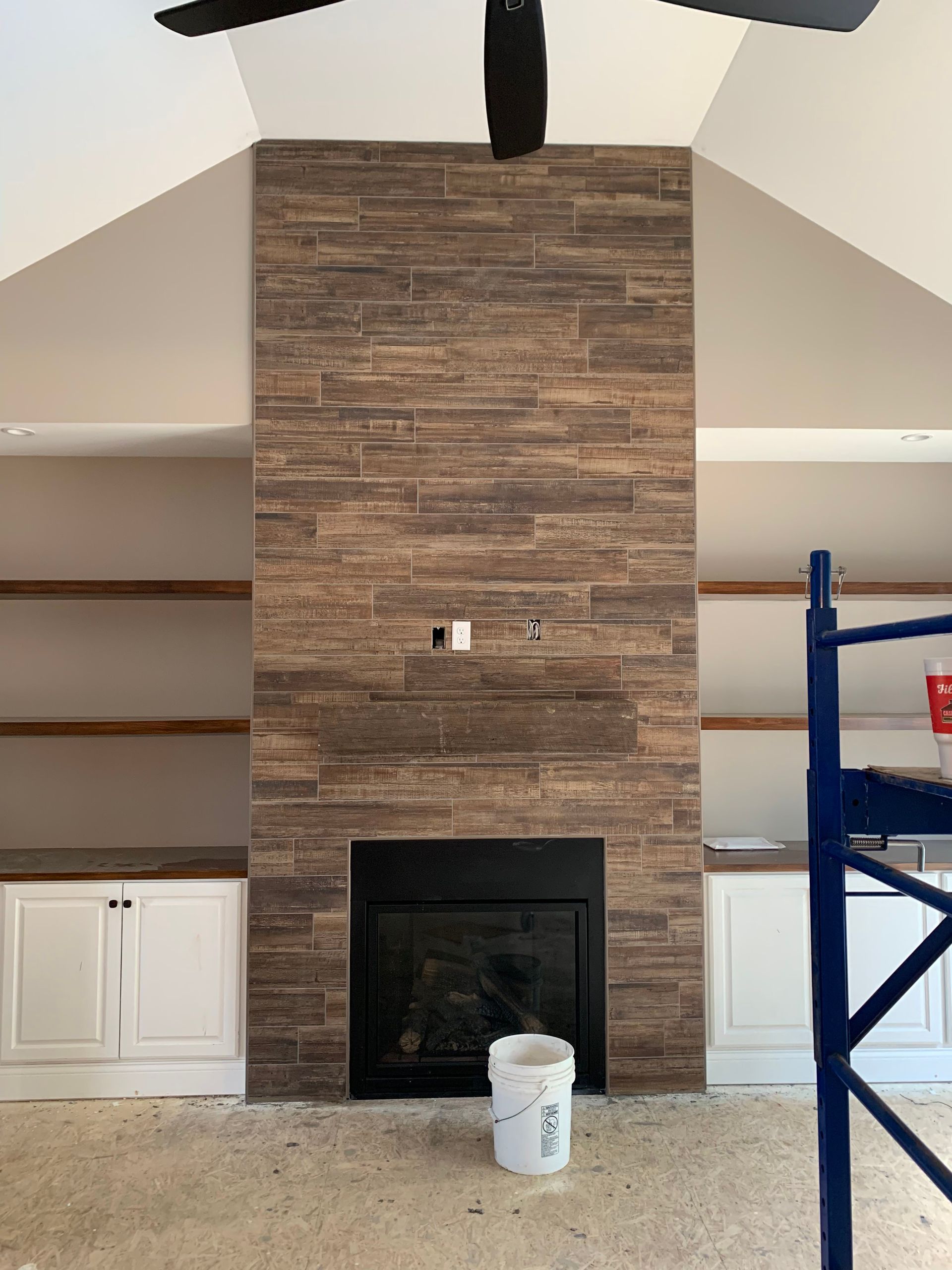 Fireplace with brown tile surround, flanked by white cabinets and shelves, unfinished room.