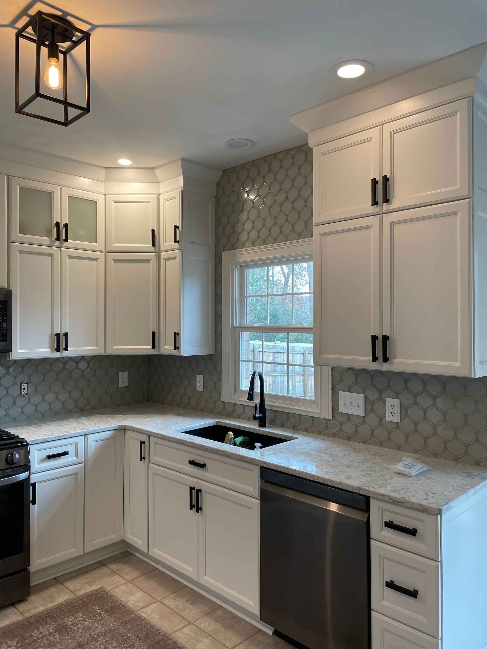 White kitchen with shaker cabinets, black hardware, granite counters, and patterned backsplash.