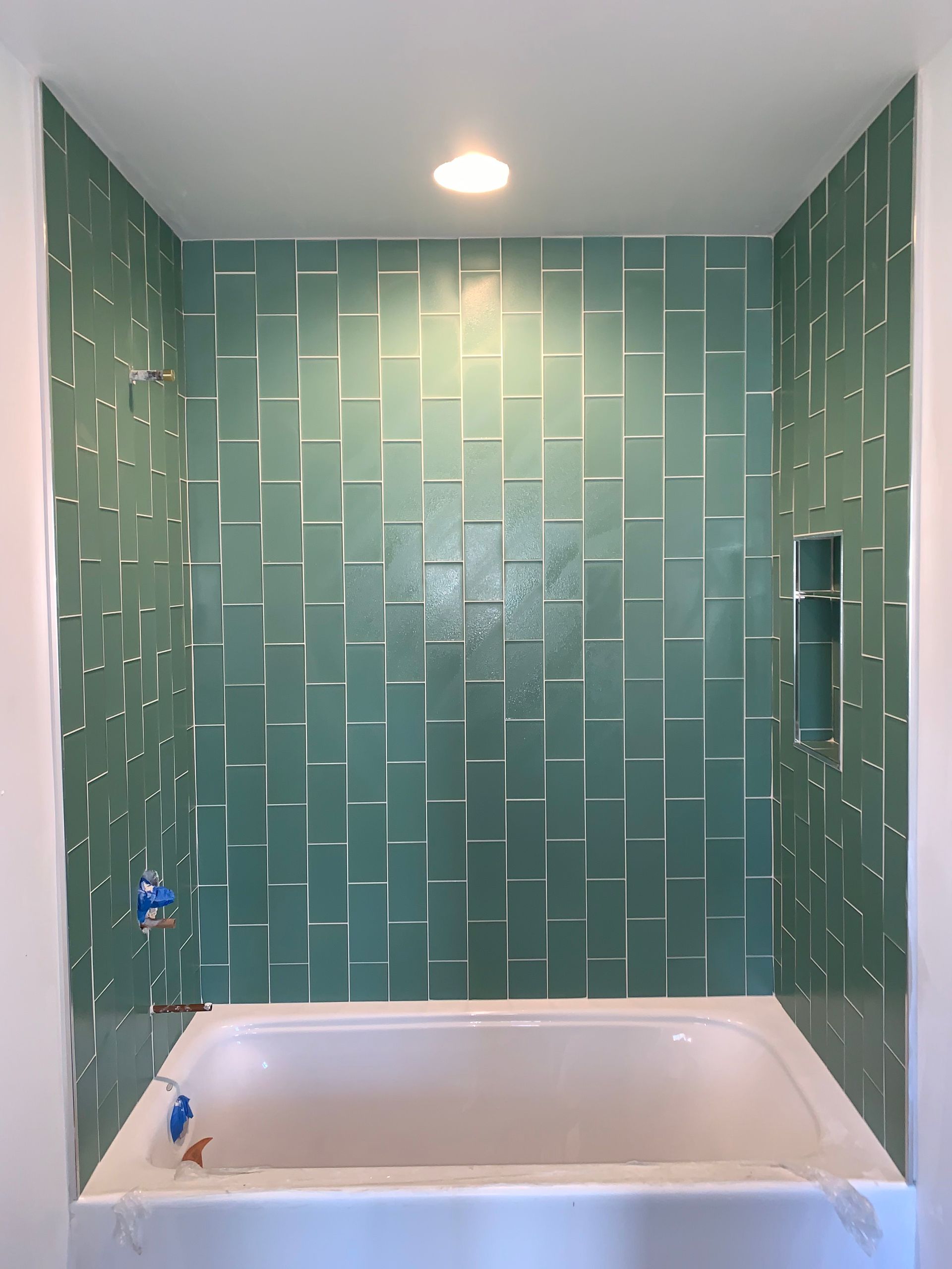 Green tiled shower surround above a white bathtub, with recessed niche.