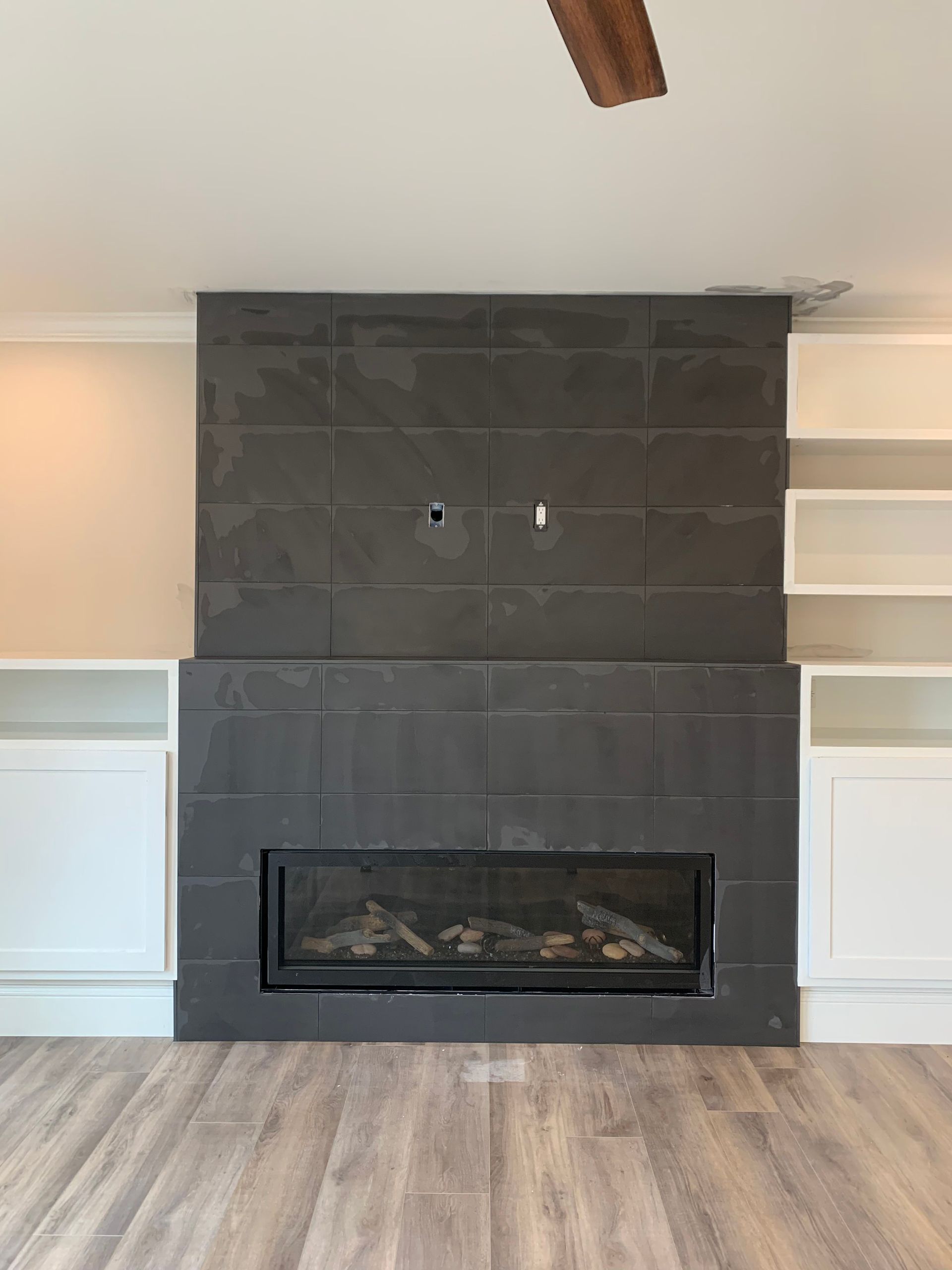 Fireplace with dark tiled surround and built-in white shelving; the room features light-colored flooring.