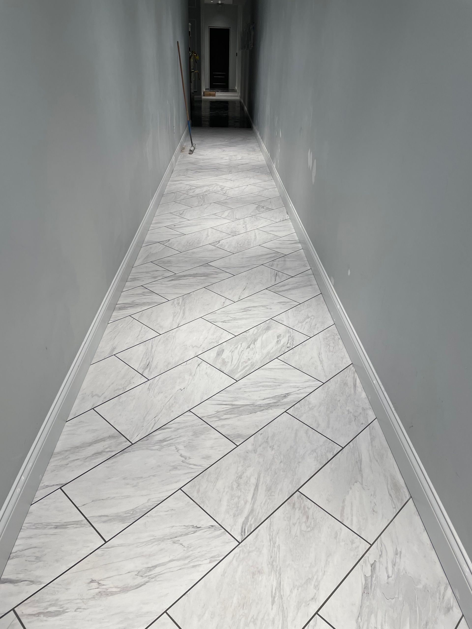 Narrow hallway with light gray walls, white tiled floor in a herringbone pattern.