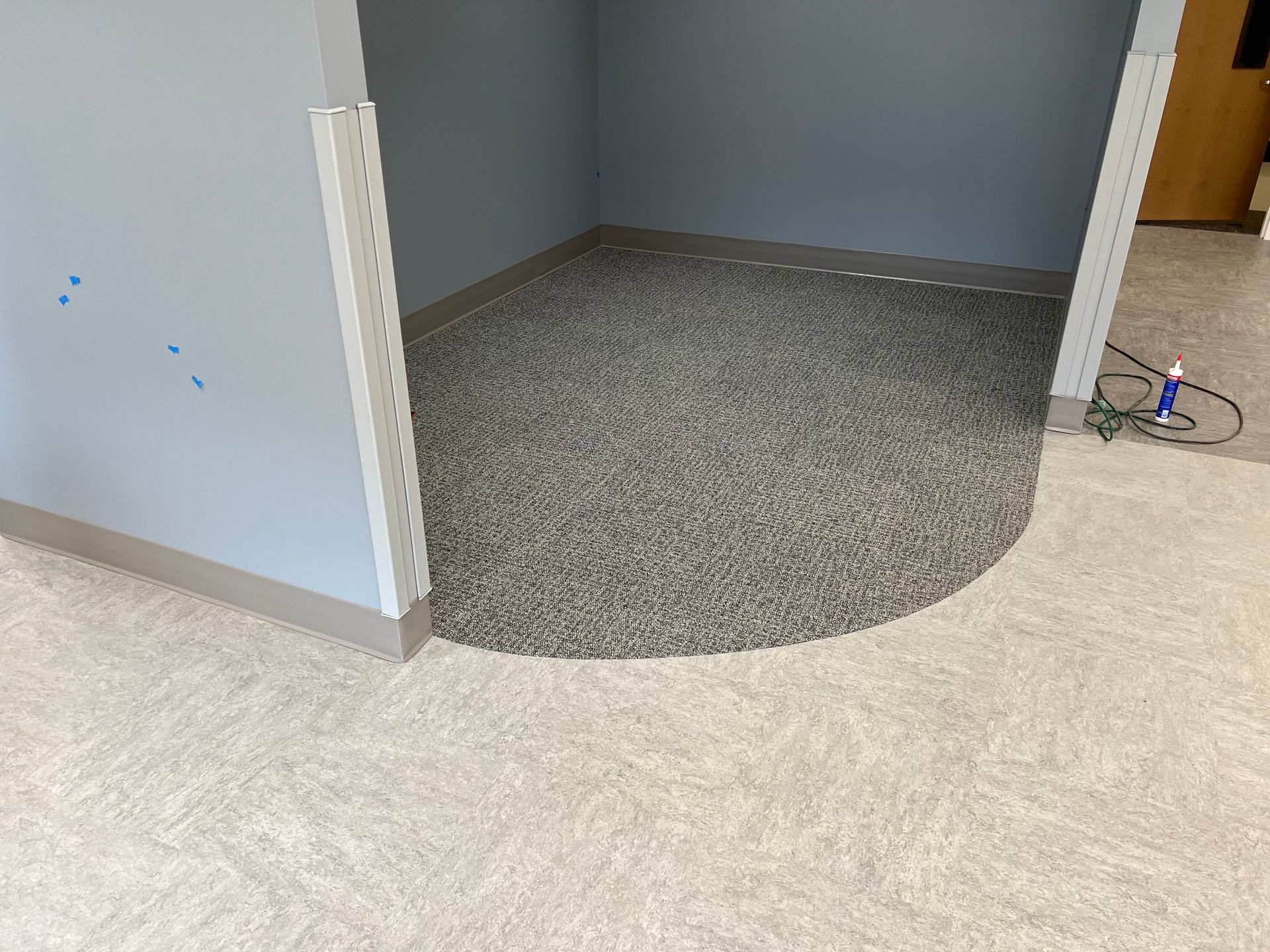 A room with light beige carpet transitions to a gray speckled floor, surrounded by blue walls and silver trim.
